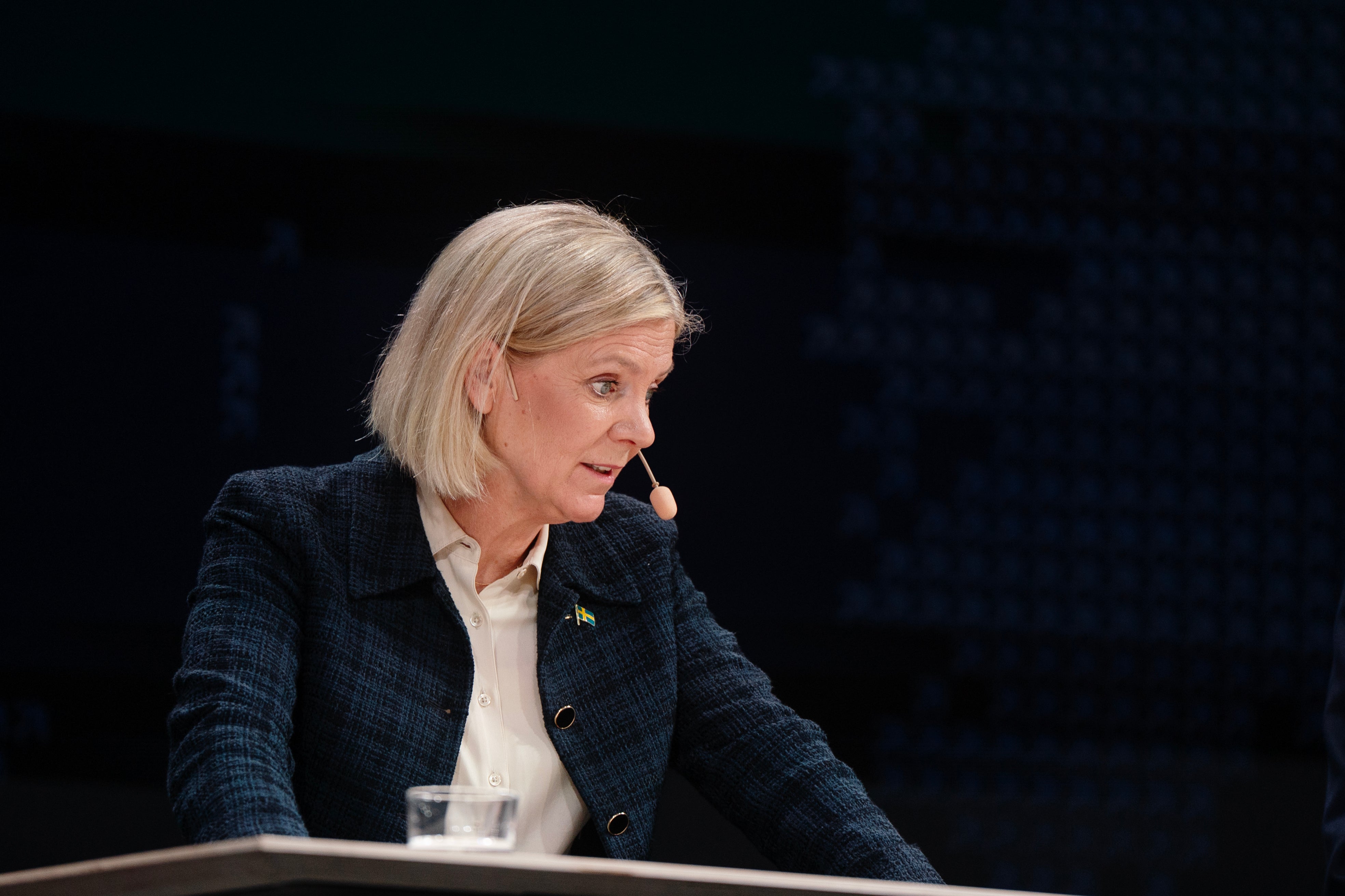 Kvinna i mörkblå kavaj sitter vid ett bord under en presentation och talar.