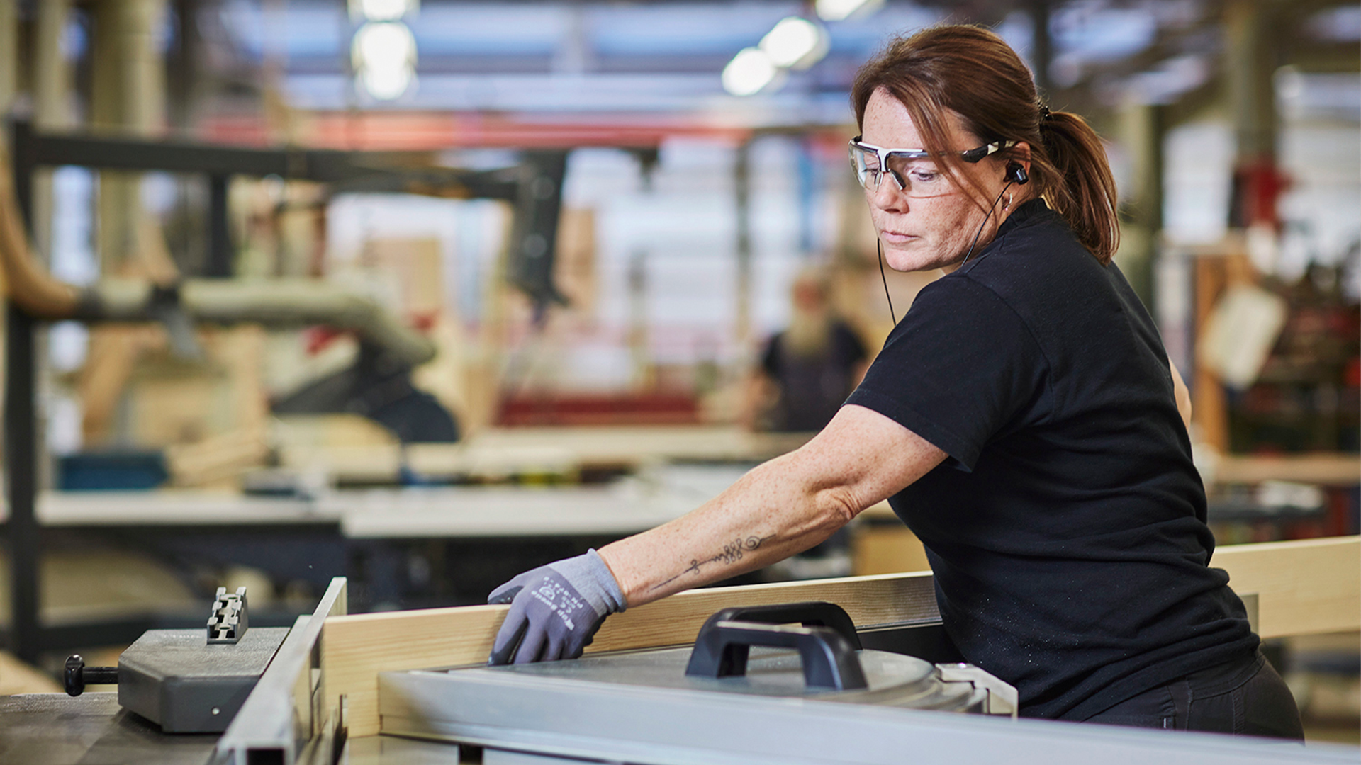 Kvinnlig arbetare i fabrik arbetar vid en arbetsbänk i en industriell miljö.