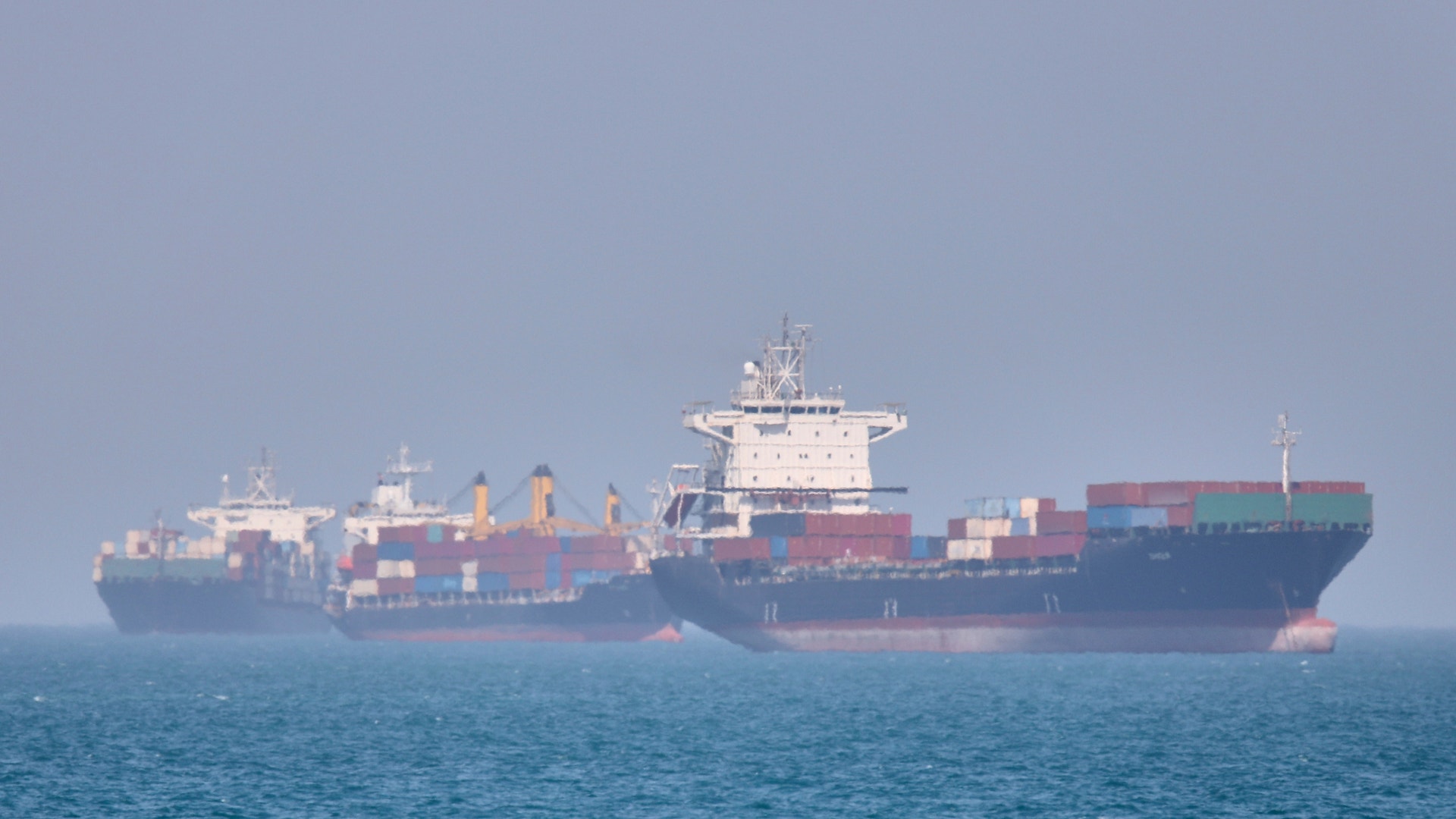 Containerfartyg på öppet hav med färgglada lastcontainrar staplade på däck.
