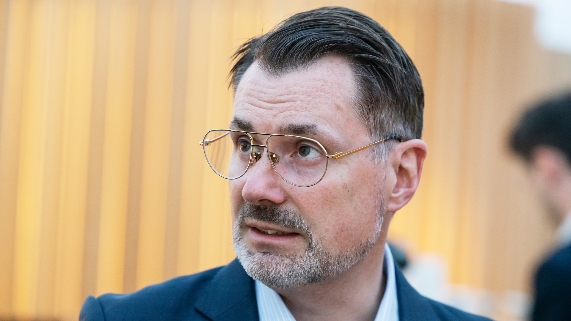 Porträtt av en man i kavaj och glasögon som tittar åt sidan.