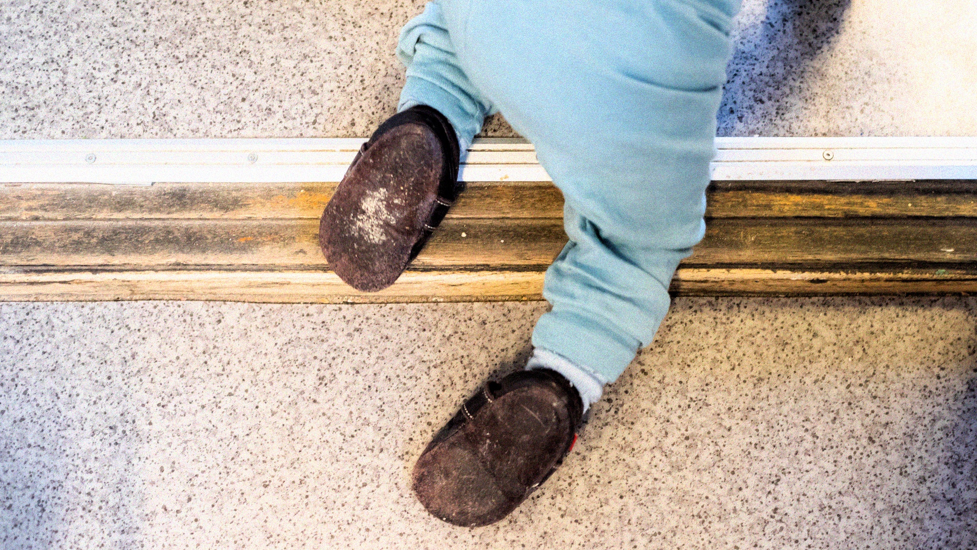 Barn i ljusblå byxor och mörka skor står på en tröskel