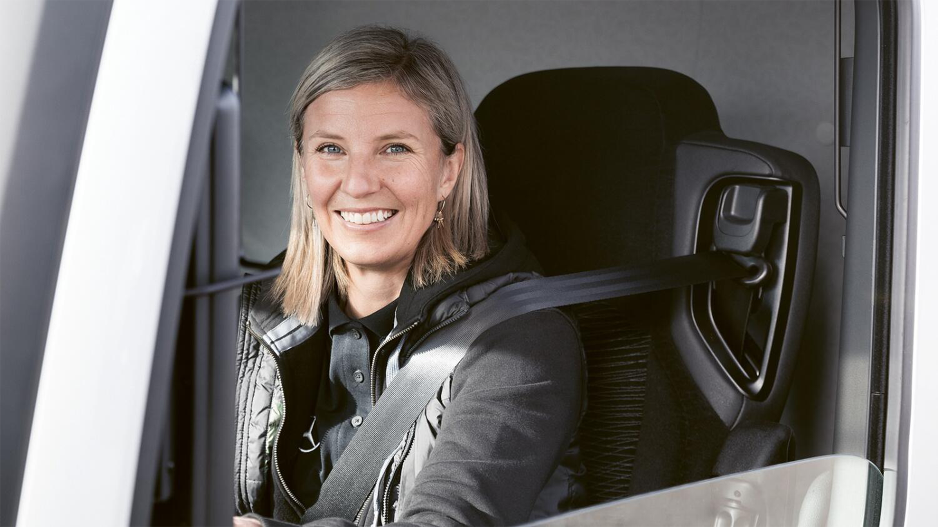 Porträtt av en kvinna som sitter i förarsätet på ett fordon och ler mot kameran.