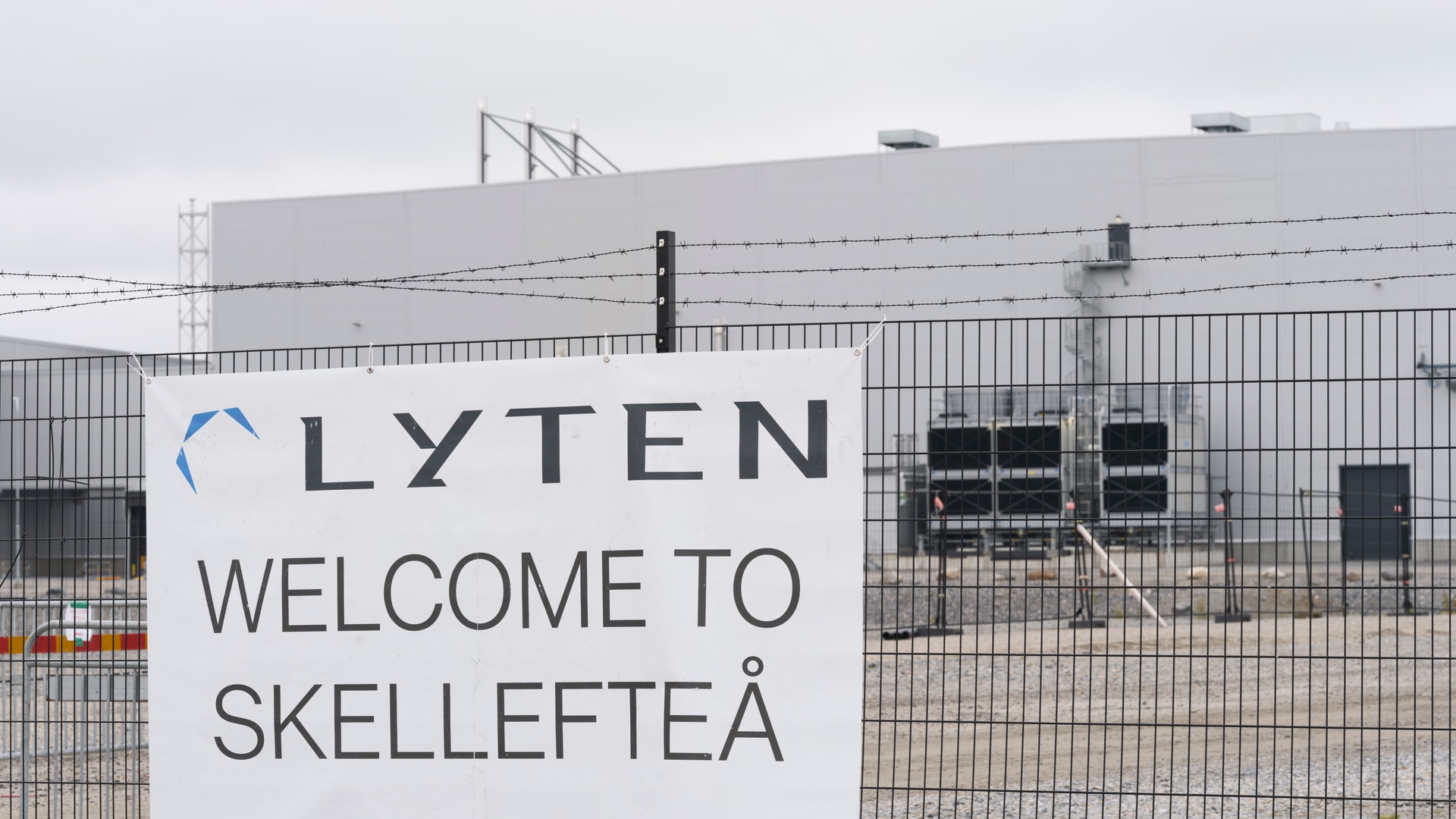 Välkomstskylt för Lyten vid en industrianläggning i Skellefteå med en stor grå fabriksbyggnad i bakgrunden.
