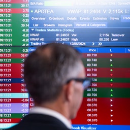 Två personer tittar på finansiella handelsdata och aktiekurser på datorskärmar.