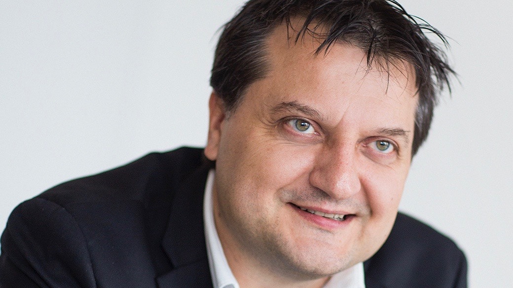 Porträtt av en man i mörk kostym och vit skjorta som ler mot kameran.