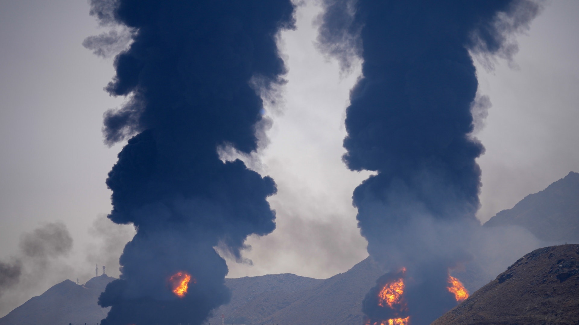 Industrianläggning med stora explosioner och flammor som skapar tjock mörk rök mot himlen.