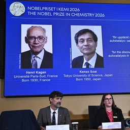 Tre personer sitter vid ett bord framför en stor skärm som visar två Nobelpristagare i kemi 2026, Henri Kagan och Kenso Soai.