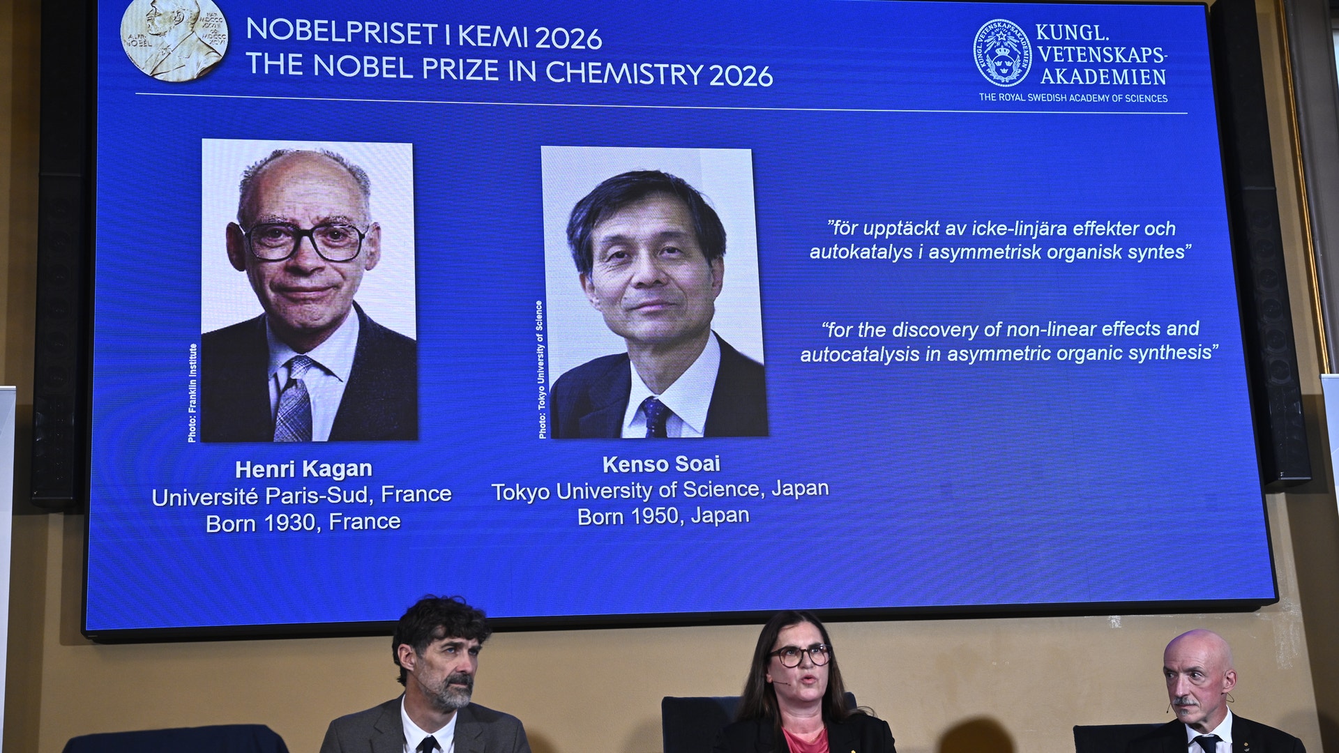 Tre personer sitter vid ett bord framför en stor skärm som visar två Nobelpristagare i kemi 2026, Henri Kagan och Kenso Soai.