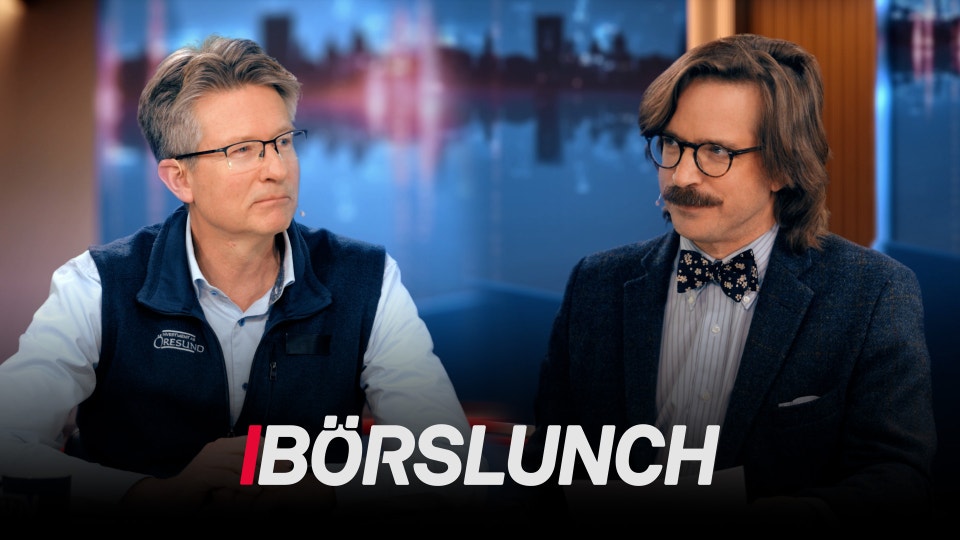 Två män i TV-studio med stadsskyline i bakgrunden