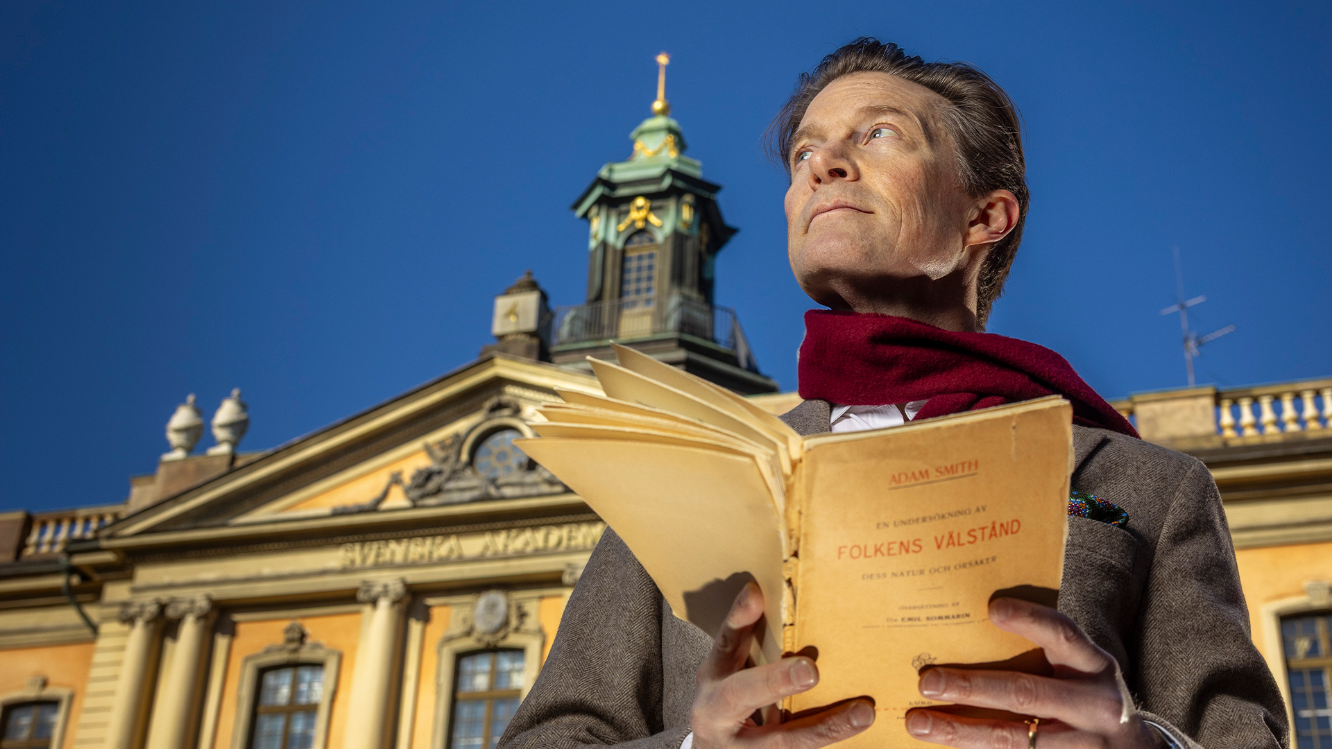 Man läser en bok framför en klassisk gul byggnad med kupol