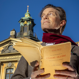 Man läser en bok framför en klassisk gul byggnad med kupol