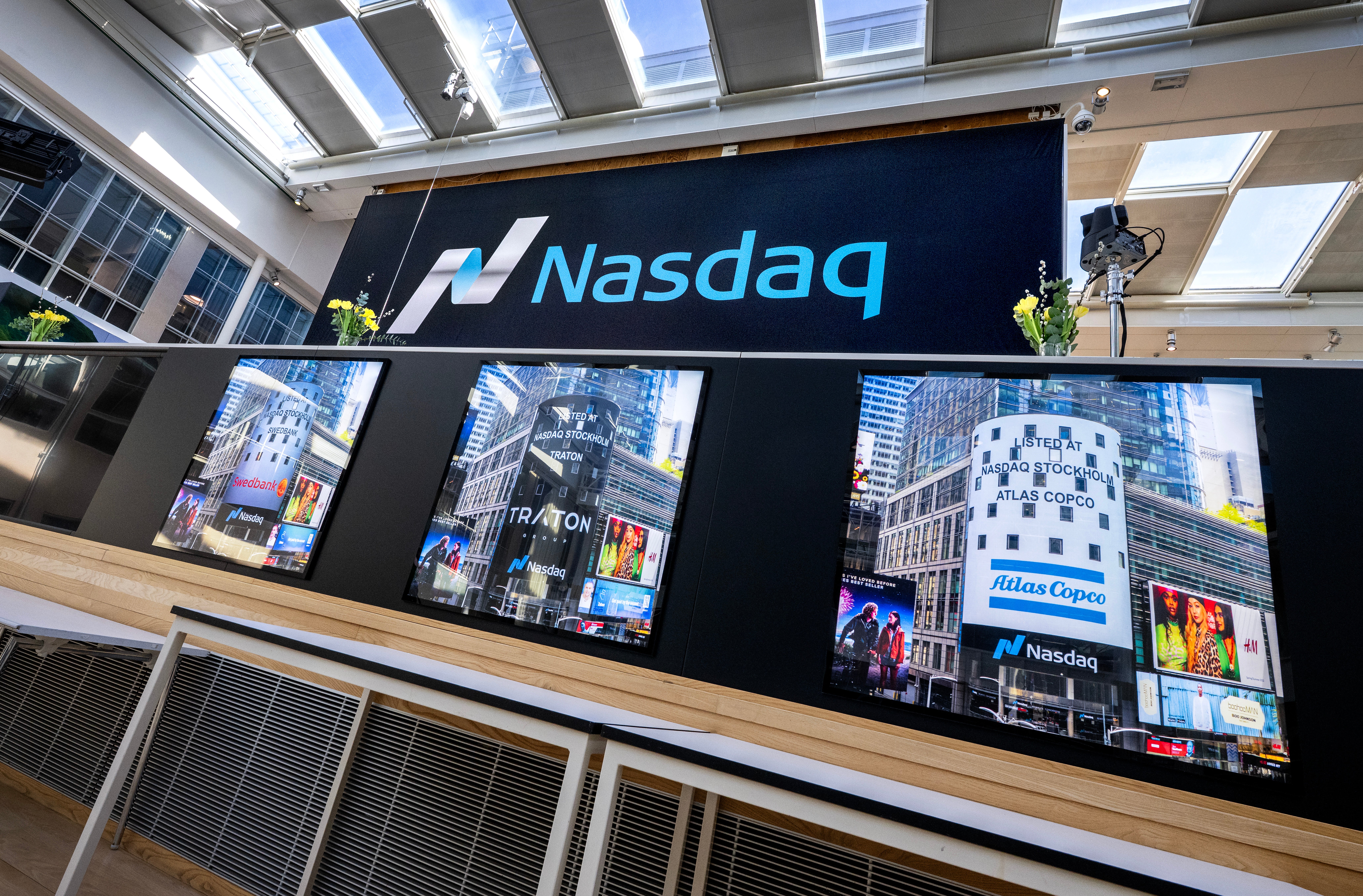 Nasdaq-logotyp och displayskärmar på en finansiell handelsbörsa som visar marknadsdata och aktiekurser.
