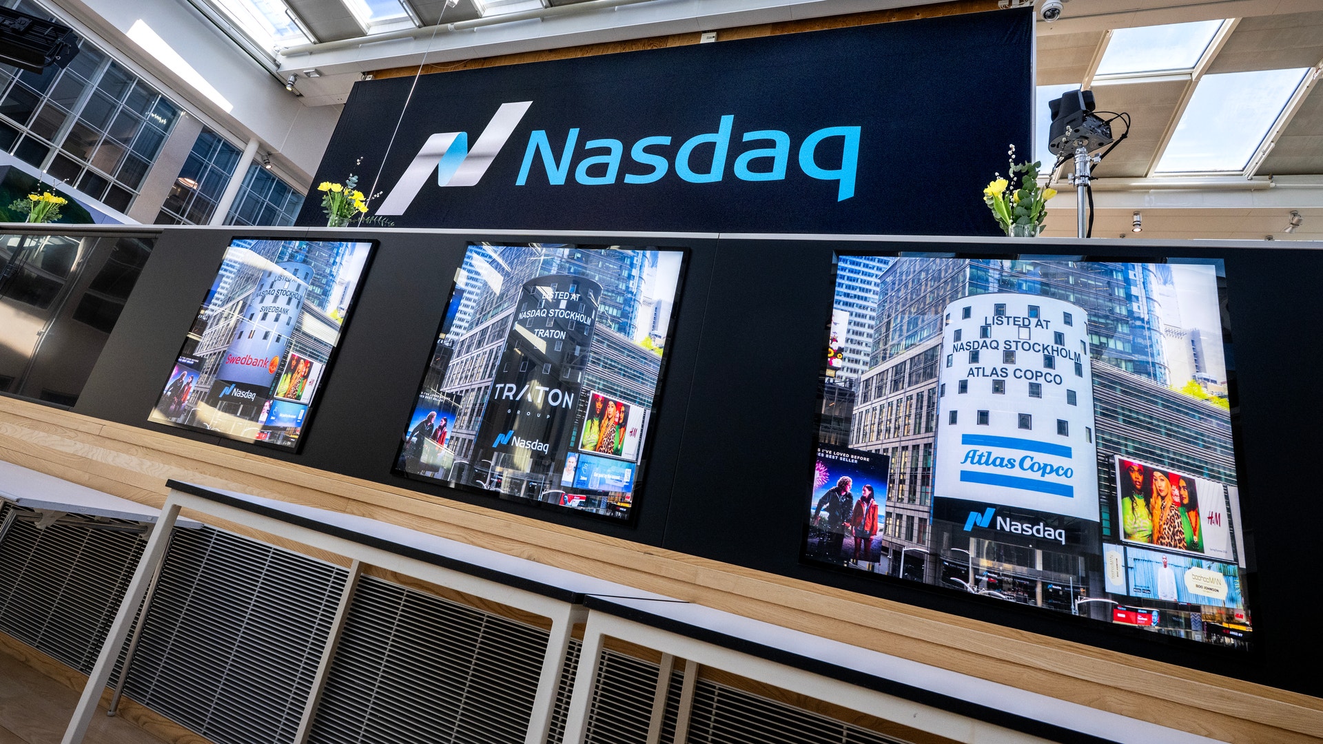 Nasdaq-logotyp och displayskärmar på en finansiell handelsbörsa som visar marknadsdata och aktiekurser.