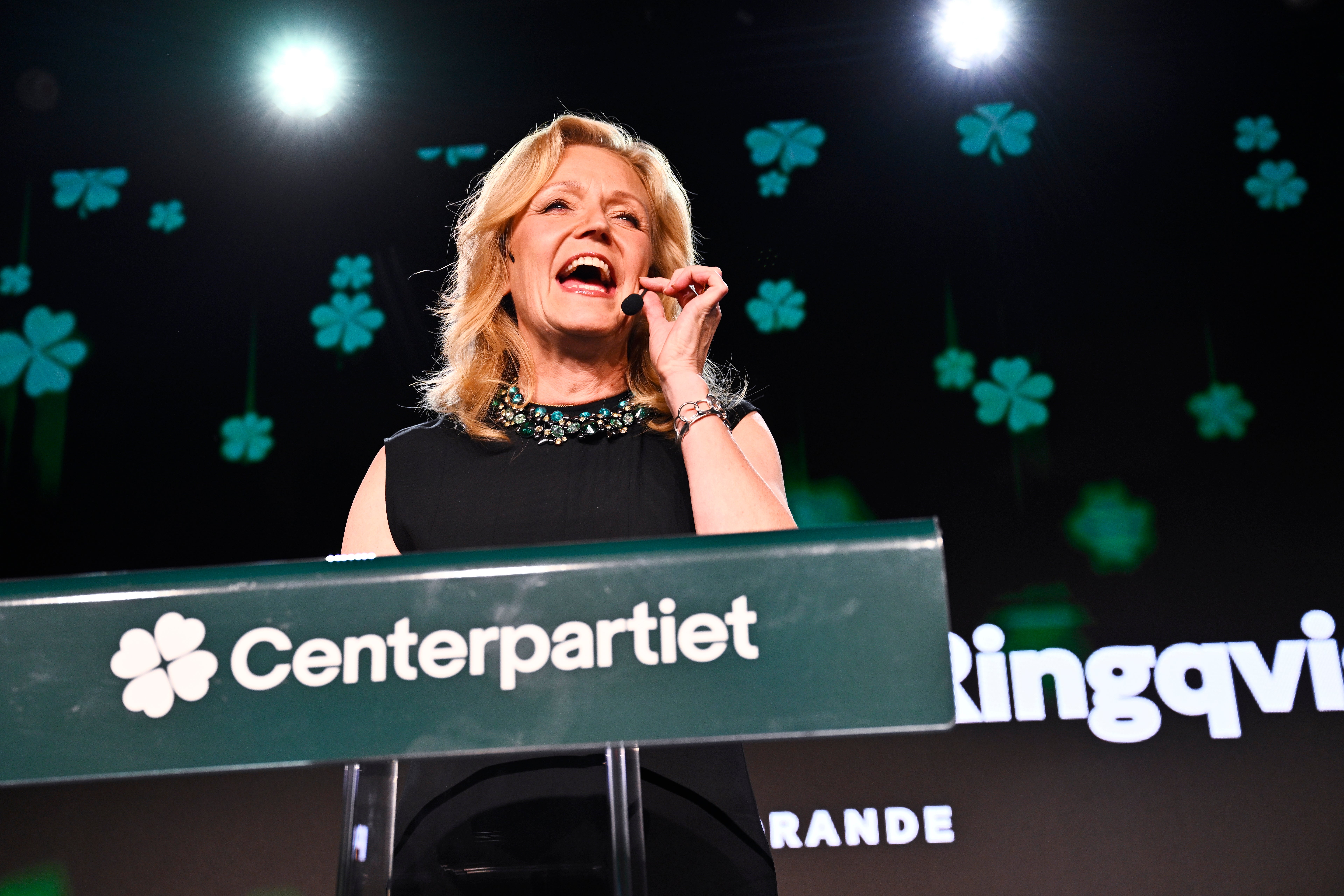 En kvinna talar engagerat vid en talarstol med Centerpartiets logotyp.