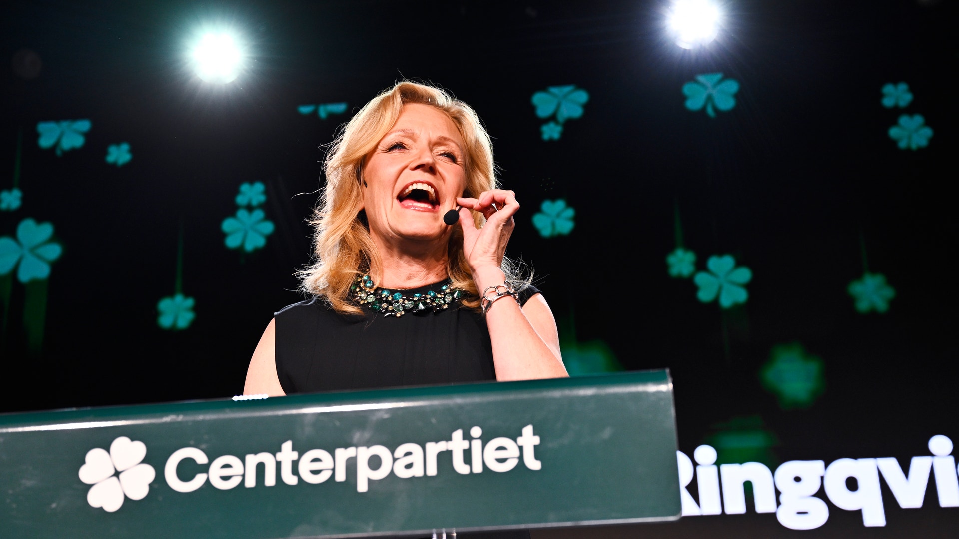 En kvinna talar engagerat vid en talarstol med Centerpartiets logotyp.