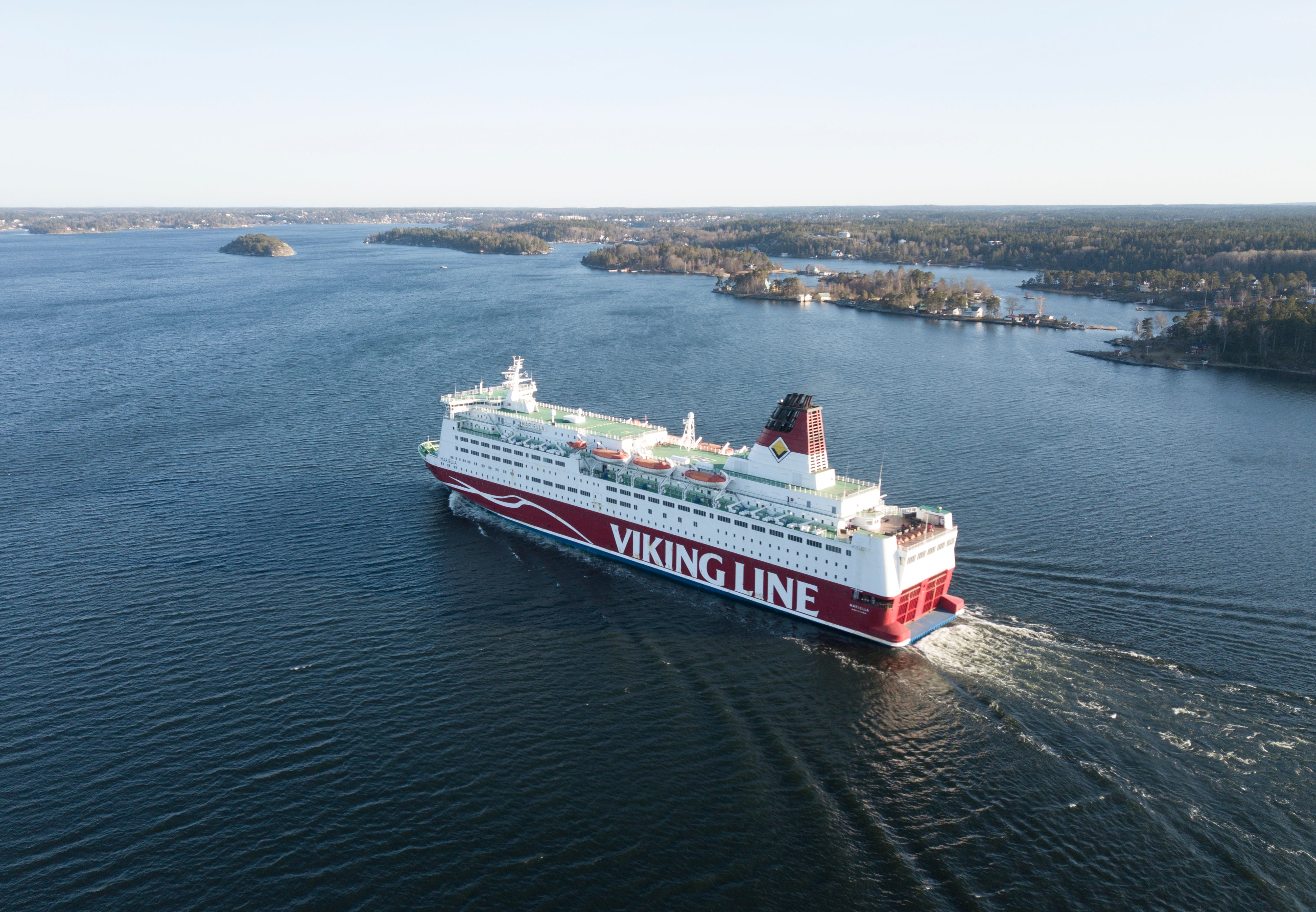 Flygbild av en vit och röd Viking Line-färja som seglar genom en skärgård en klar dag.