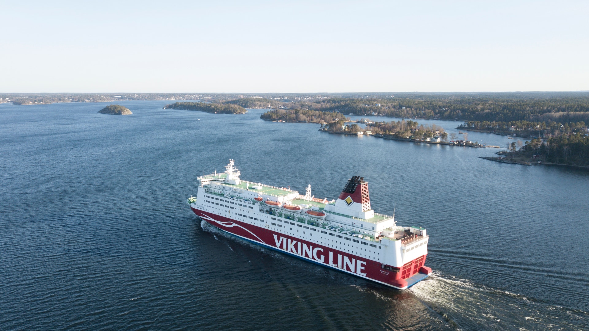 Flygbild av en vit och röd Viking Line-färja som seglar genom en skärgård en klar dag.