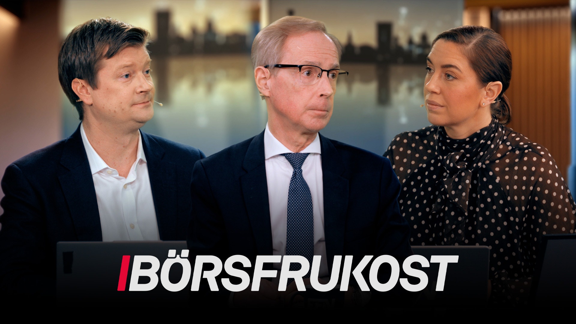 Tre personer i affärsmiljö under en börsfrukost-event, med stadsutsikt i bakgrunden.