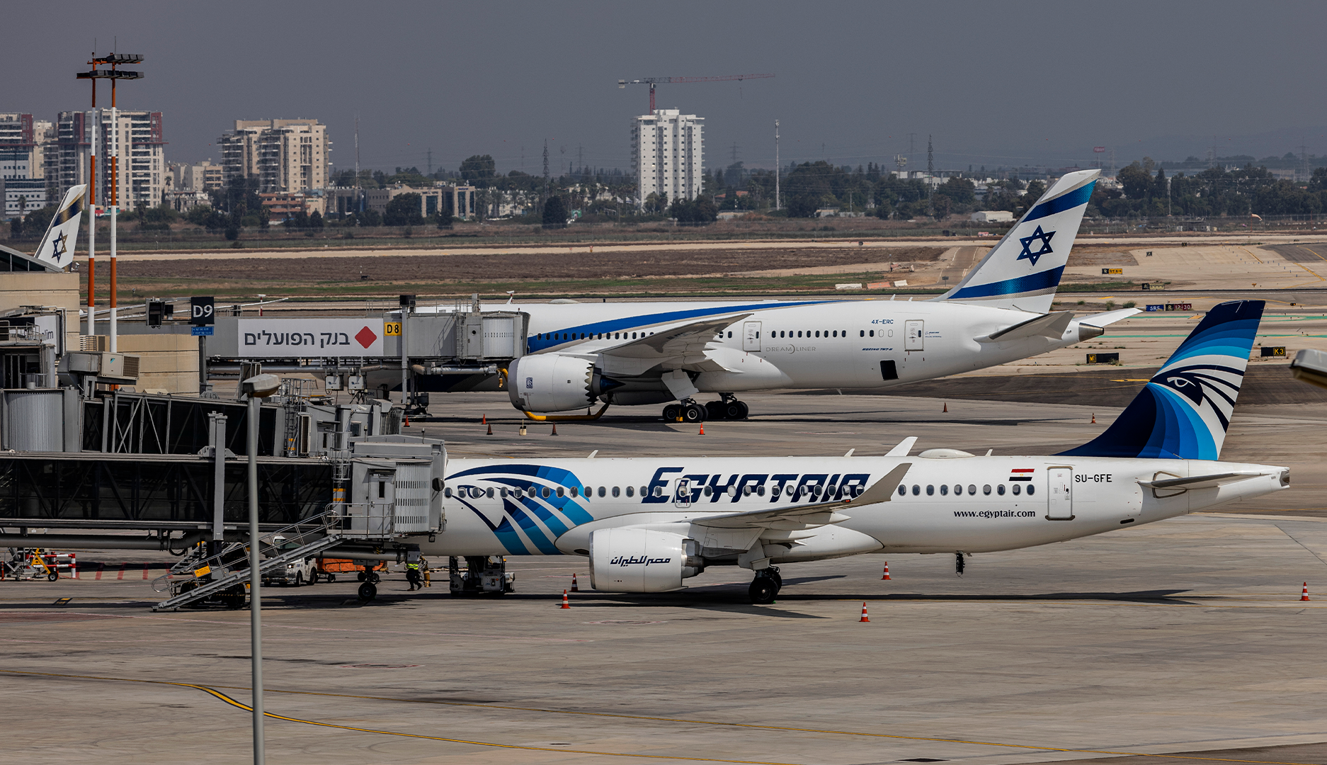 Två passagerarflygplan på en flygplats. I förgrunden en EgyptAir-maskin och bakom den ett El Al-plan. Flygplatsens byggnader och stadssiluett syns i bakgrunden.