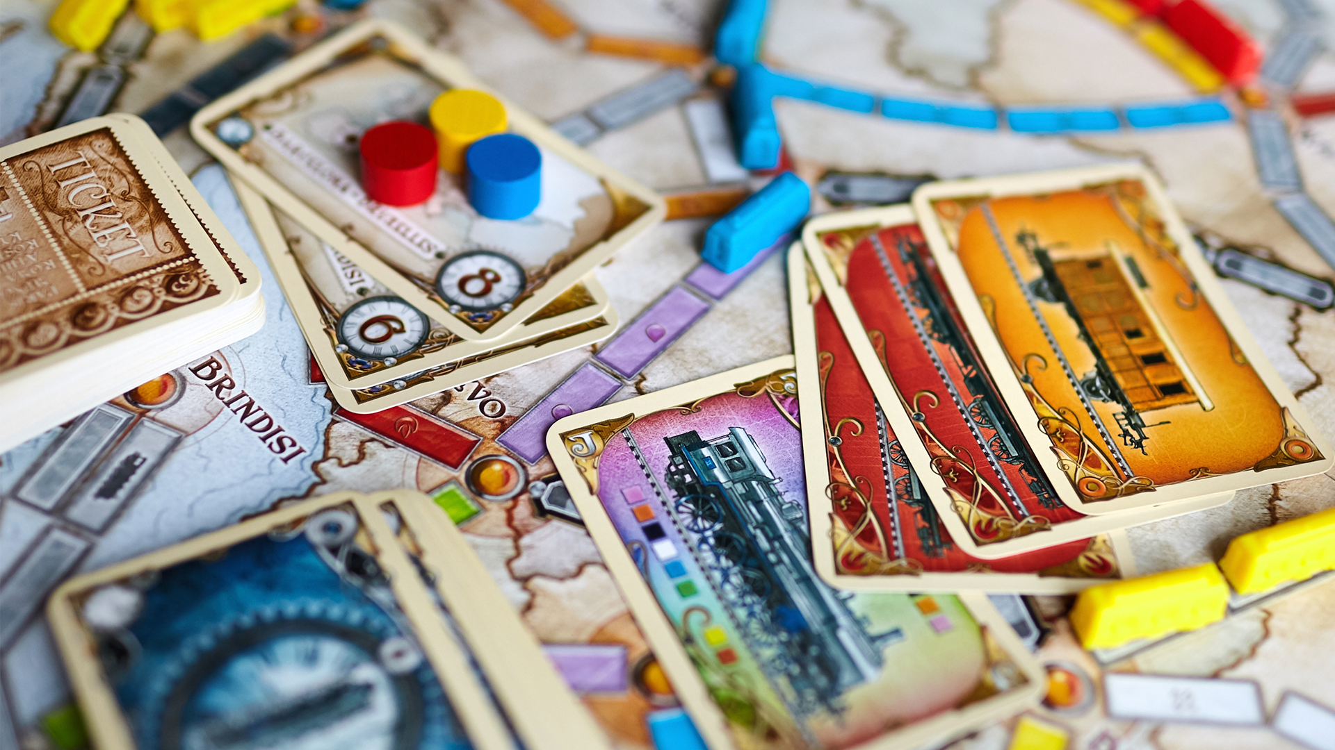 Närbild av brädspelet Ticket to Ride med spelbräde, färgglada tågkort i röd, gul och blå, träfärgade spelbrickor och en blå spelbricka synlig på spelplanen