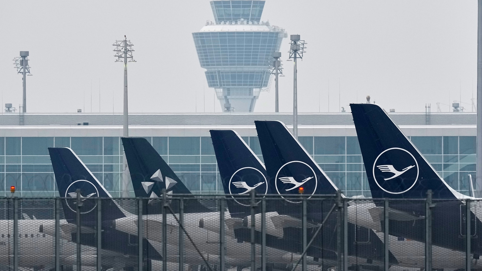 Flera flygplan parkerade vid en flygplats med en terminalbyggnad i bakgrunden.