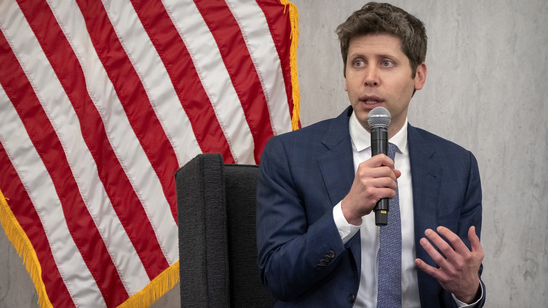 Man i kostym talar vid mikrofon framför amerikansk flagga