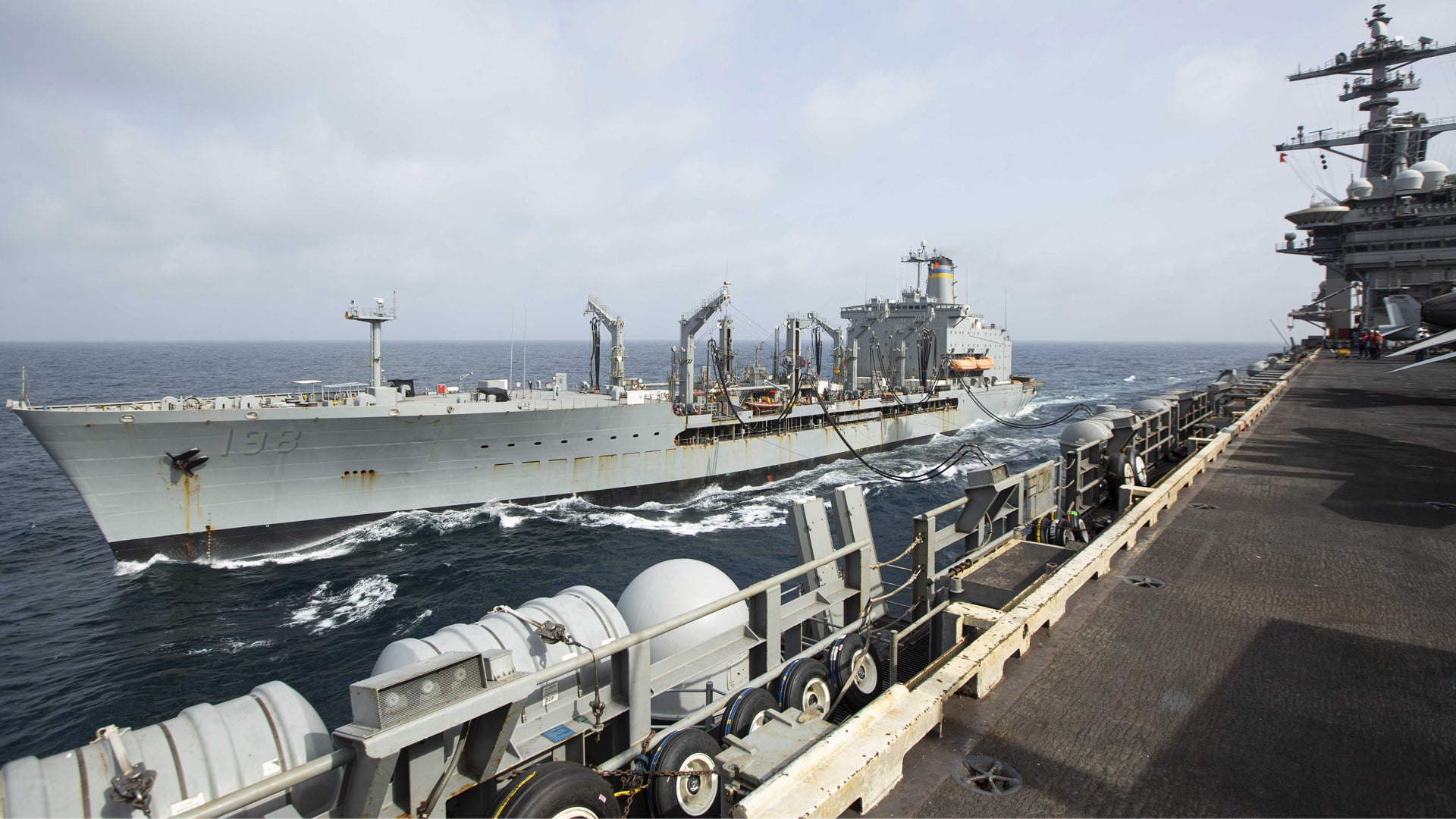 Två militära fartyg förtöjda bredvid varandra på havet med lastningsekipment synligt mellan dem.