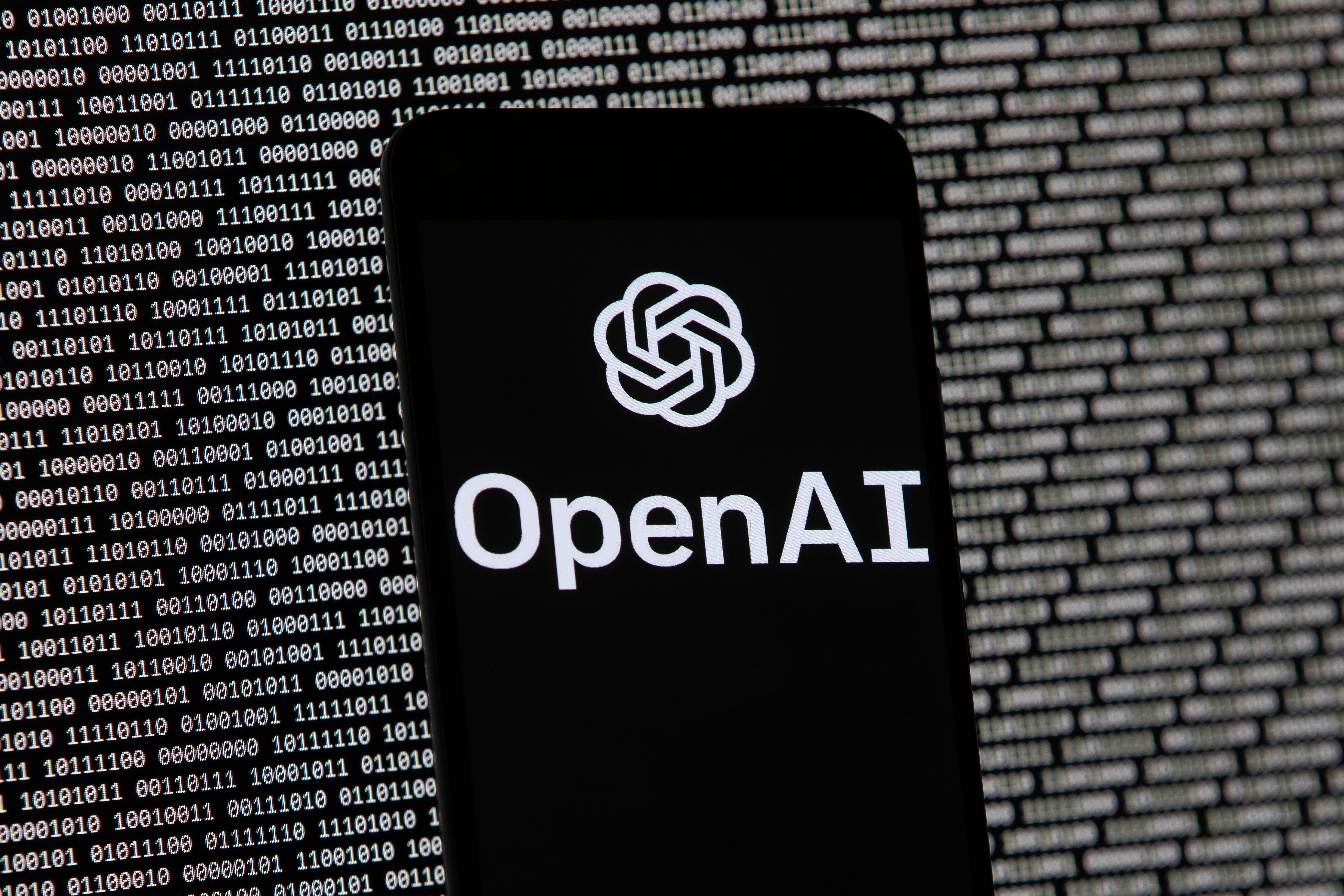 En mobiltelefon visar OpenAI:s logotyp mot en bakgrund med binär kod.