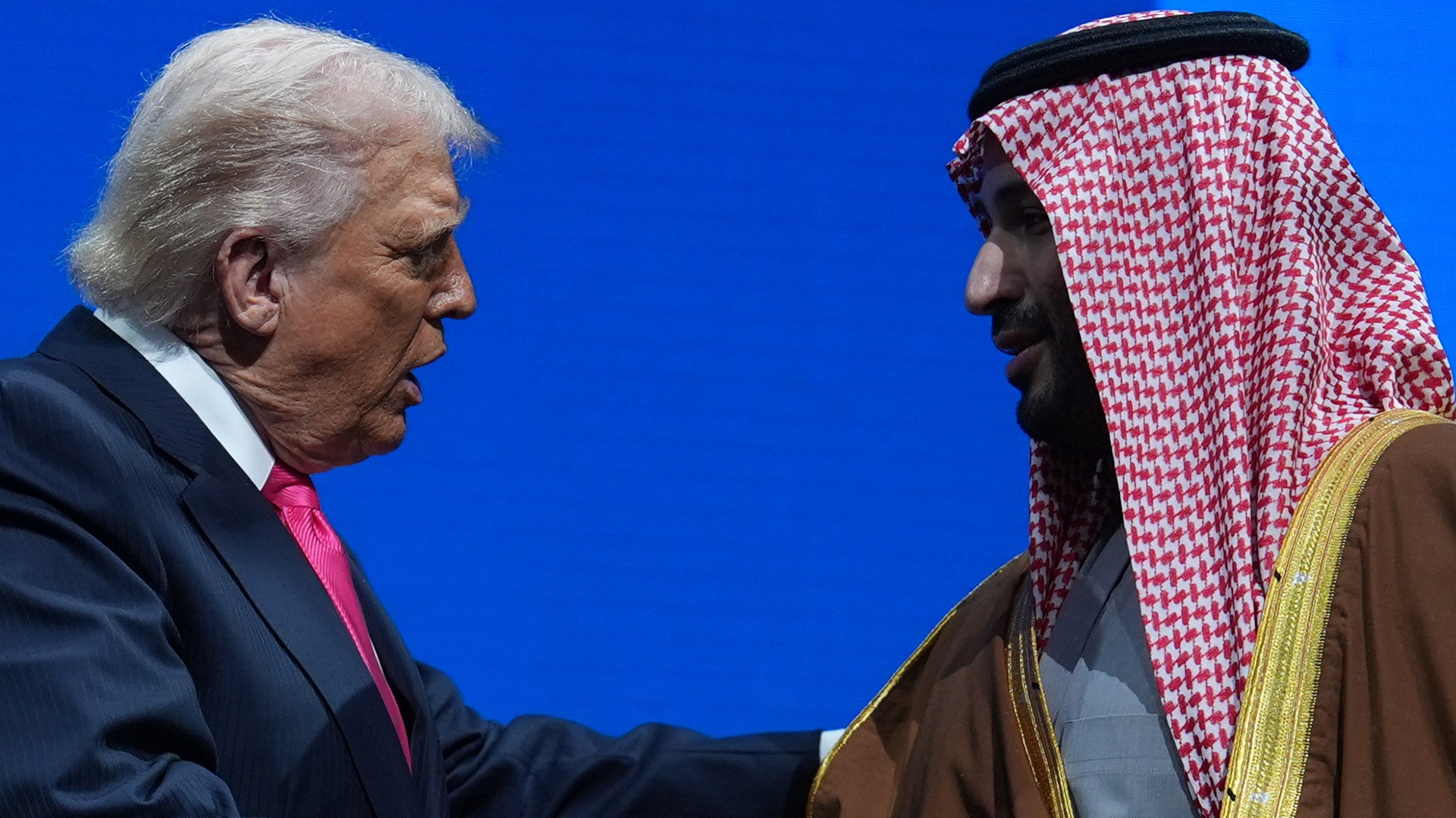 Två män i formell klädsel möts mot en blå bakgrund.