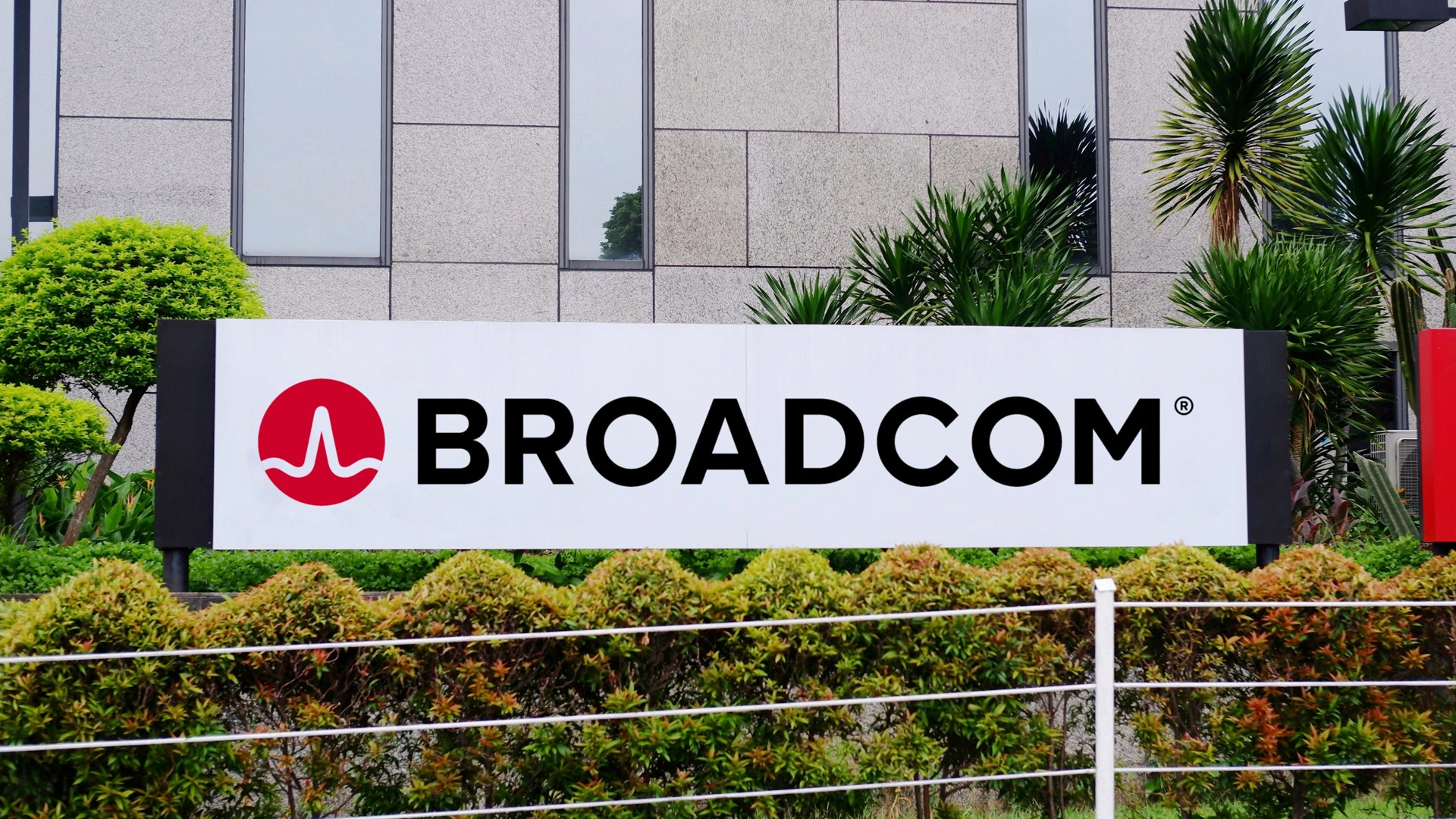 Broadcom-skylt framför en modern byggnad med gröna växter och palmer.