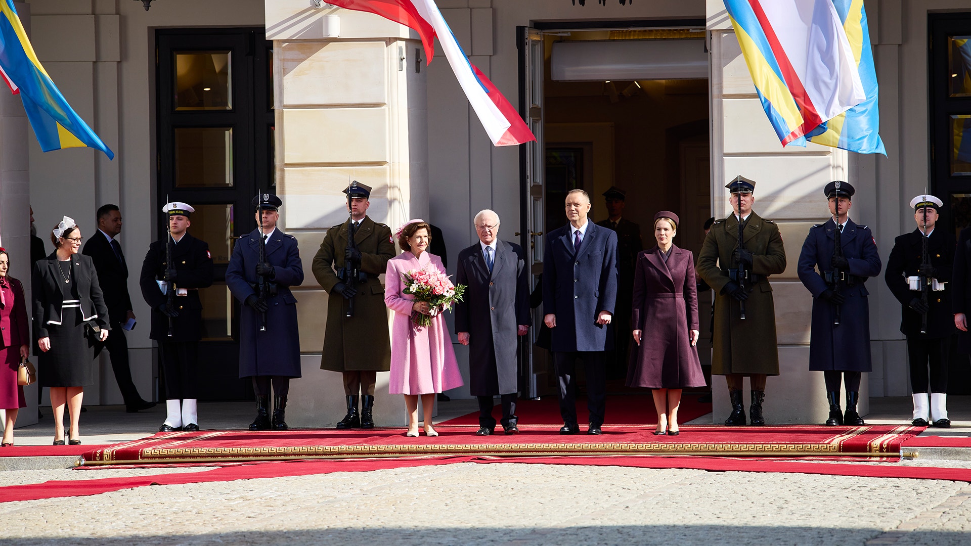 Officiell ceremoni med politiker och militär personal framför en formell byggnad med flaggor