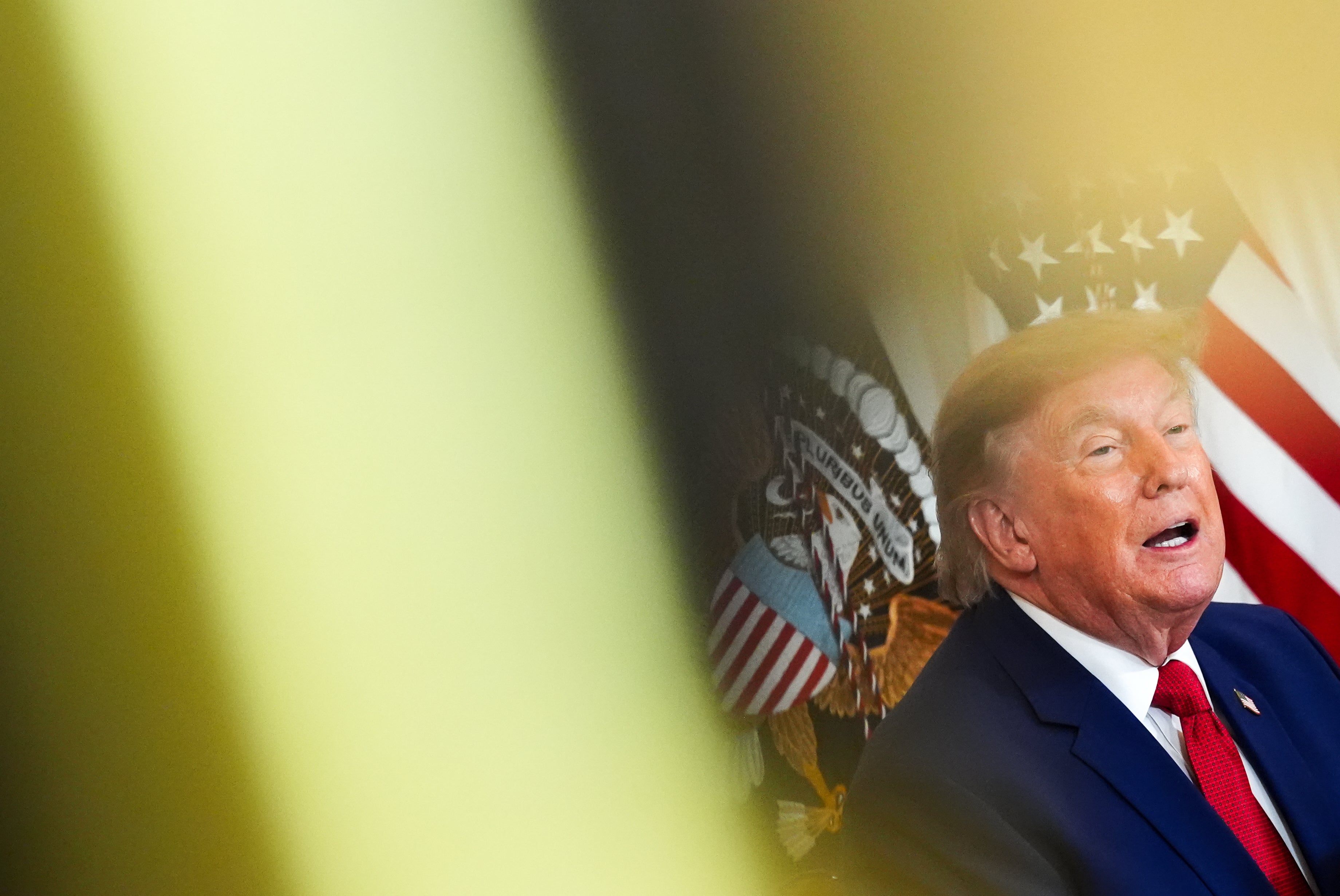 Man i mörk kostym och röd slips framför amerikanska presidentsiegeln och flaggan.