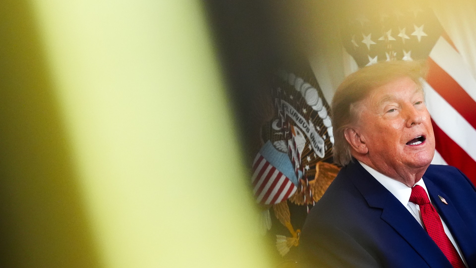 Man i mörk kostym och röd slips framför amerikanska presidentsiegeln och flaggan.