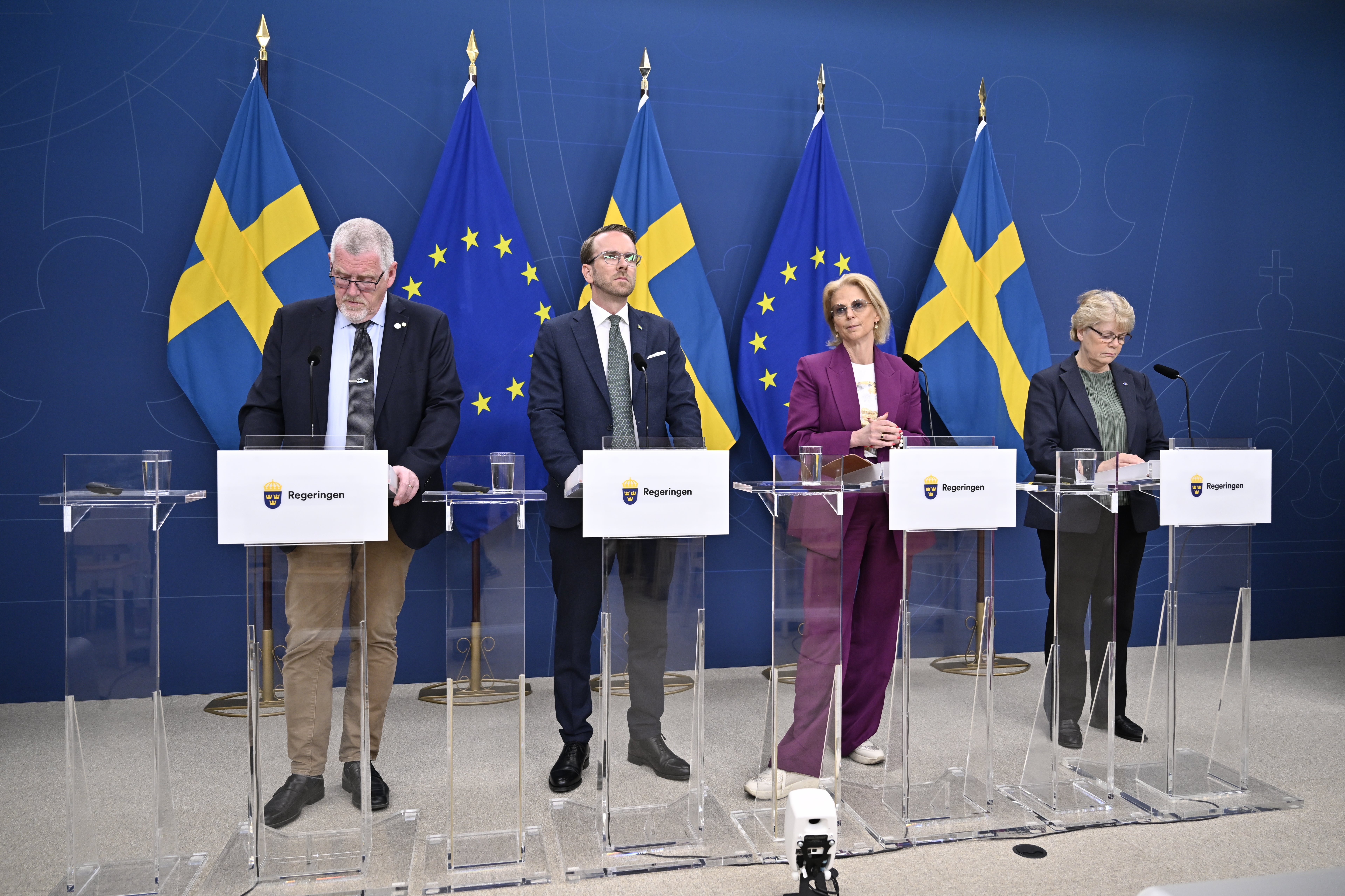 Fyra personer står vid podier under en presskonferens. I bakgrunden syns svenska flaggor och EU-flaggor på en blå vägg.