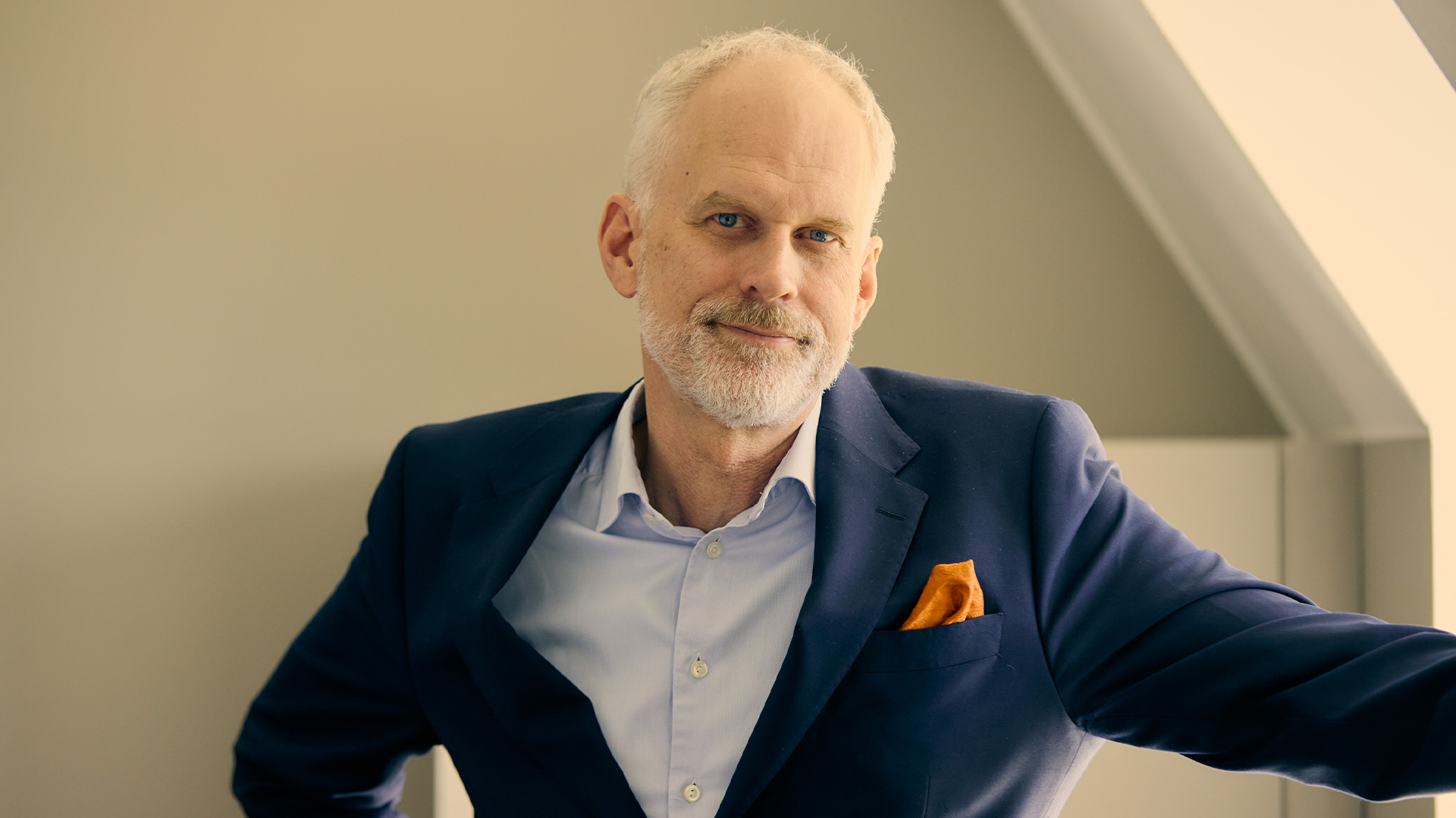 Porträttfoto av en äldre man med vit skägg, klädd i mörkblå kavaj och ljusblå skjorta