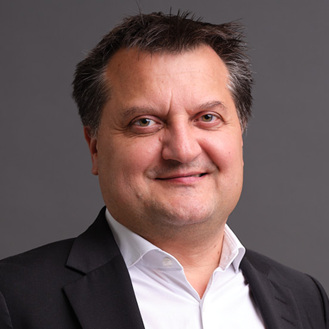 Porträtt av en man i mörk kavaj och vit skjorta mot grå bakgrund