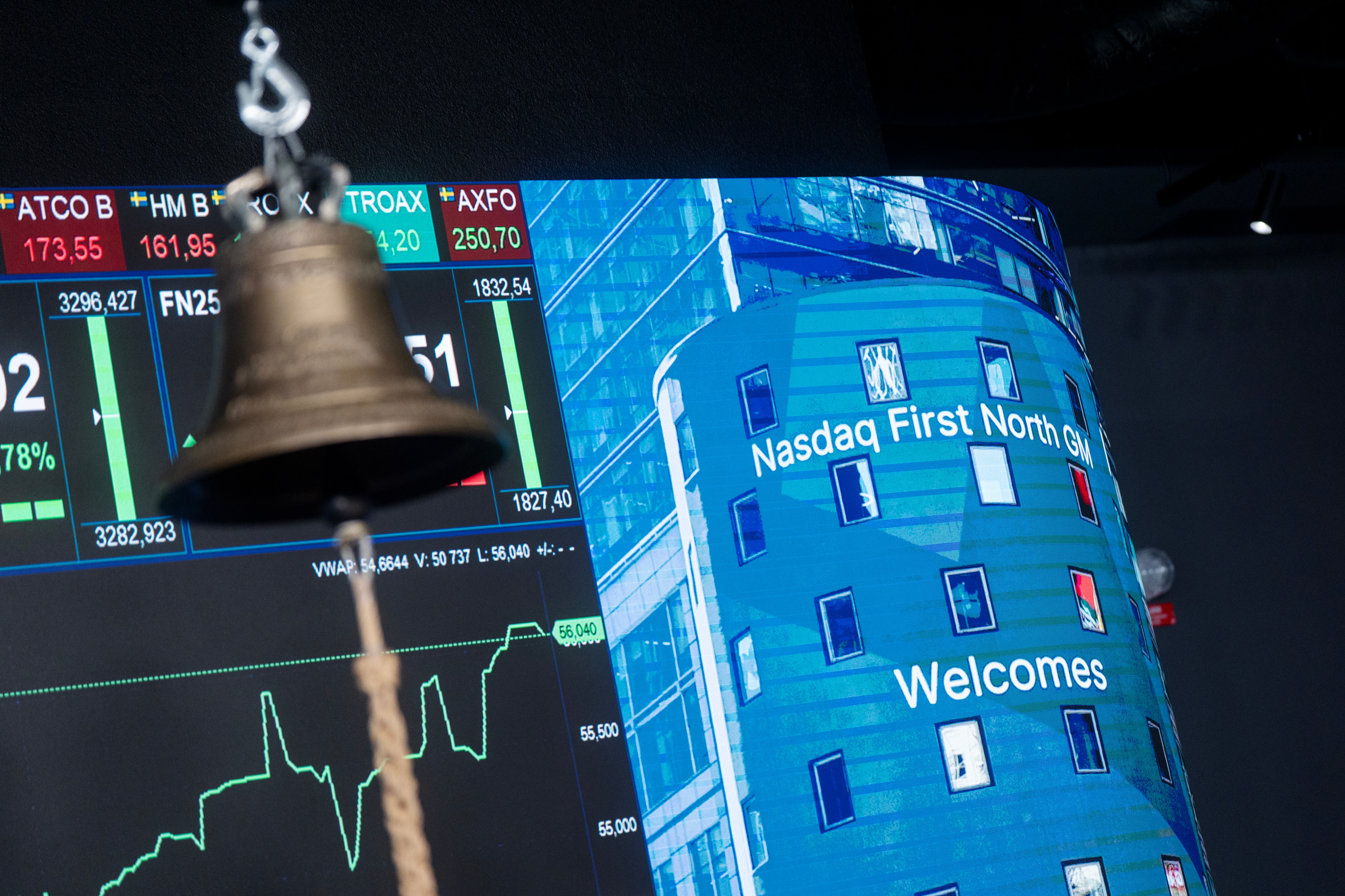 En börsklocka framför en digital skärm som visar aktiekurser och en välkomsthälsning från Nasdaq First North.