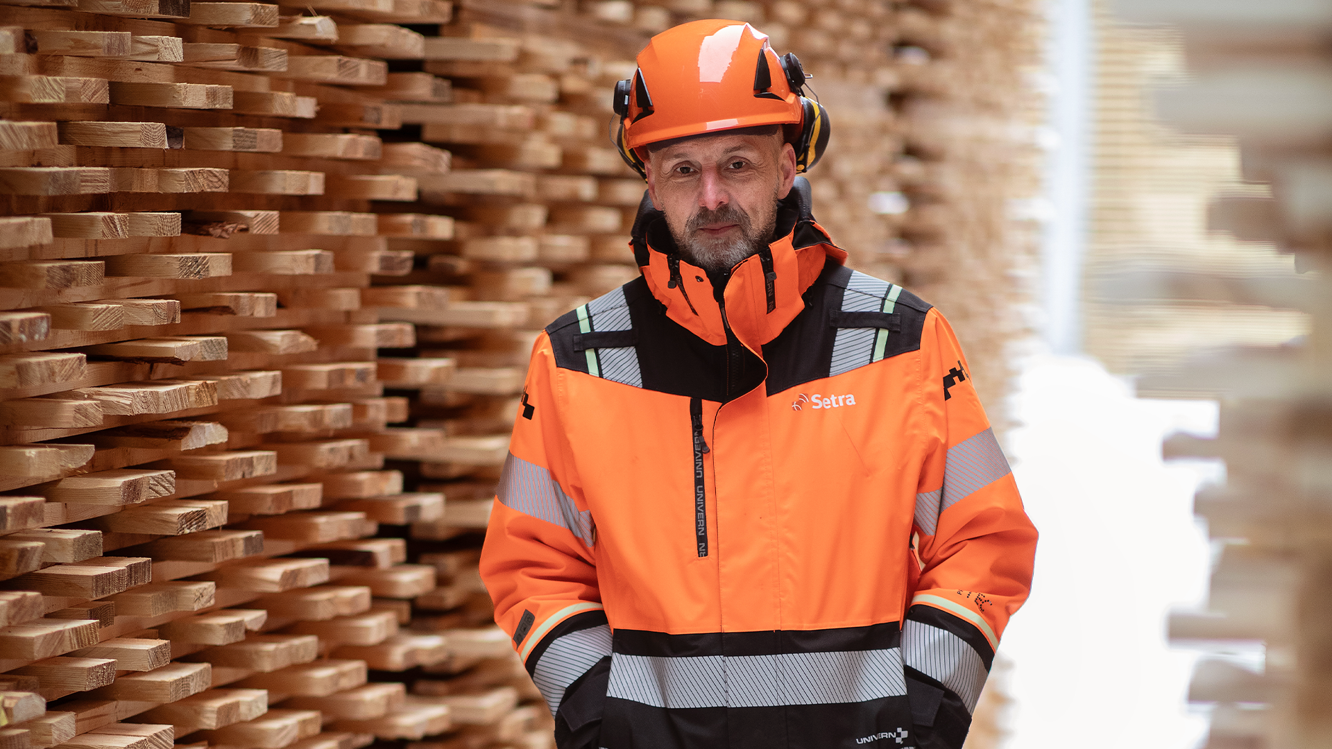 En arbetare i orange säkerhetsutrustning framför staplade träplankor