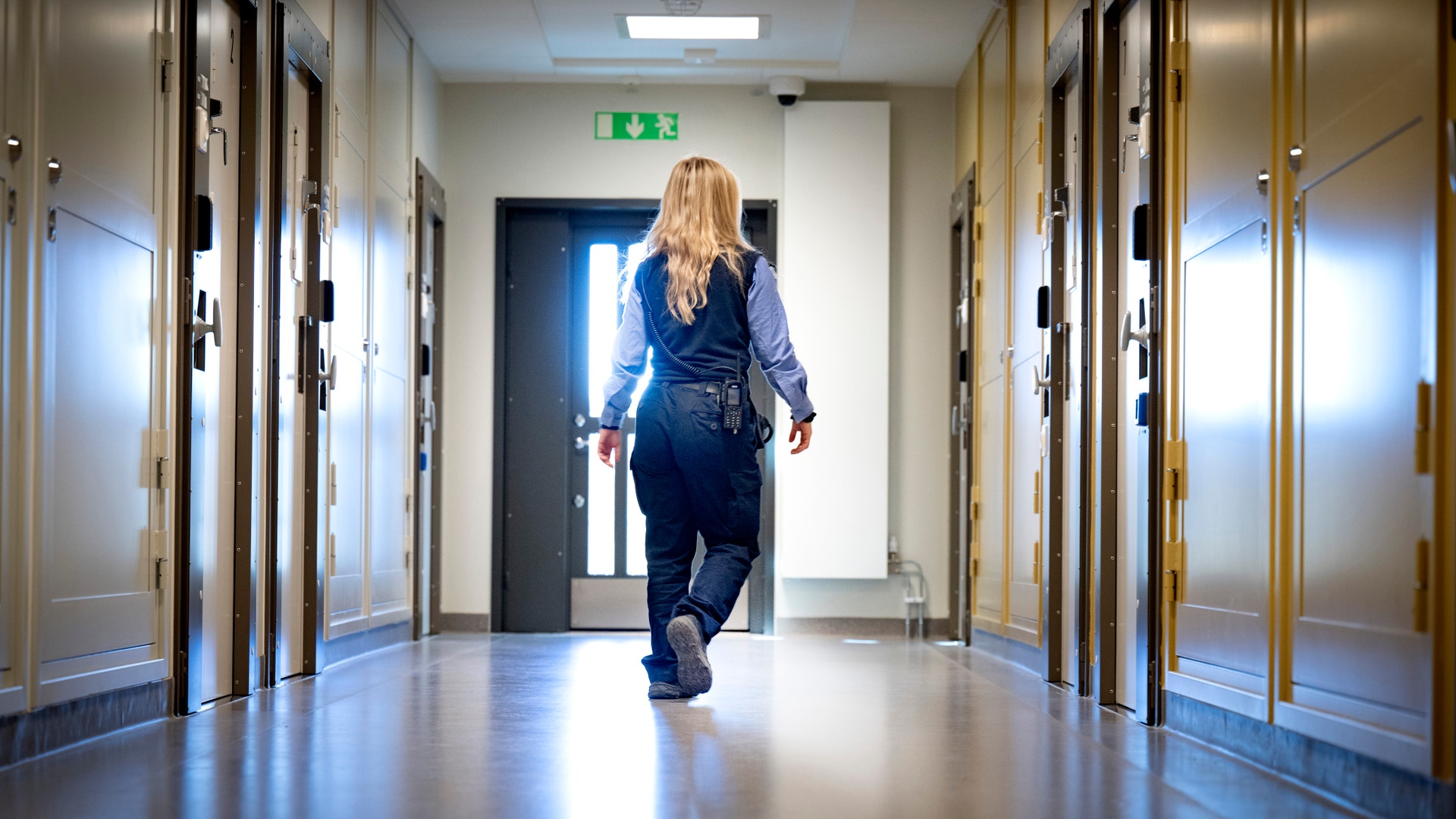En kvinnlig vårdare i uniform går längs en korridor i ett fängelse.