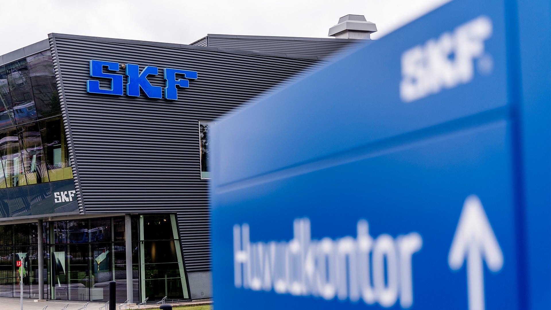 SKF:s huvudkontor. En modern byggnad med SKF-logotypen på fasaden och en blå skylt med texten Huvudkontor i förgrunden.