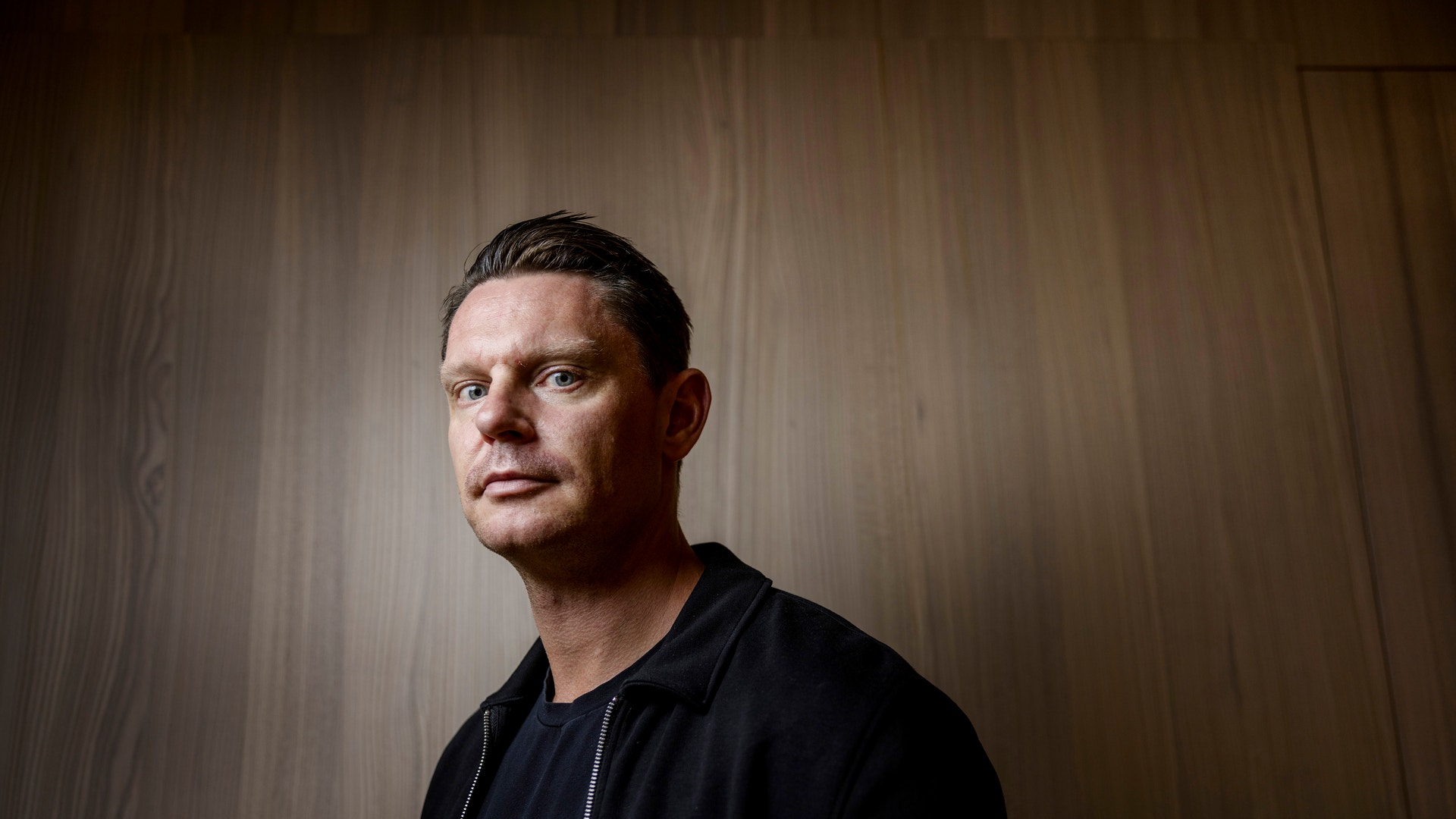 Porträttfoto av en David Sandström (marknadschef Klarna) i svart jacka mot en trävägg.