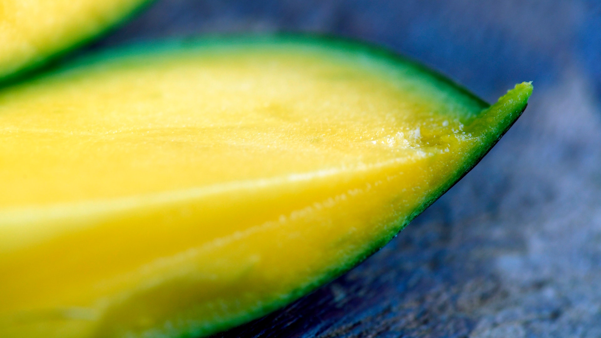 Närbild av en gul mango med grön skala på blå bakgrund
