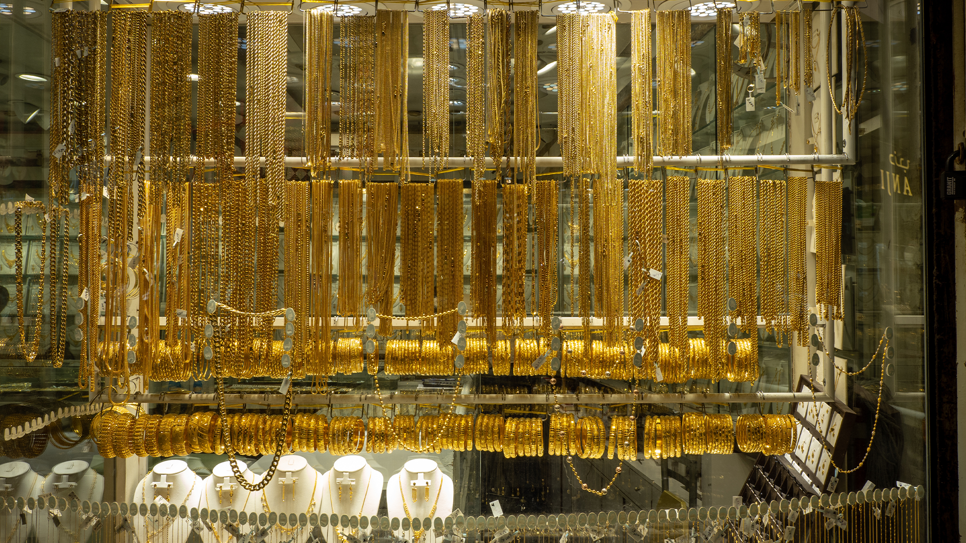 Guldsmycken på display i en juvelierbutik med guldkedjor hängande på ställ och smycken utställda på vita bystäver.
