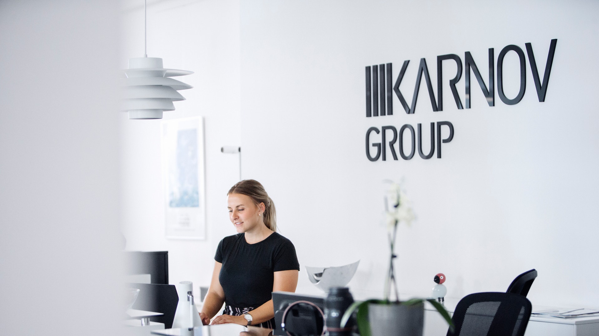 Kvinna vid ett modernt receptionssk med Karnov Group-logotyp på väggen bakom henne.