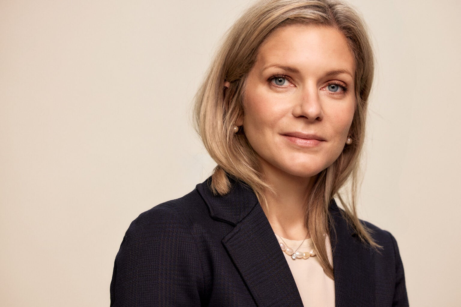 Porträtt av en kvinna med blont hår, iklädd mörkblå blazer och vit topp.