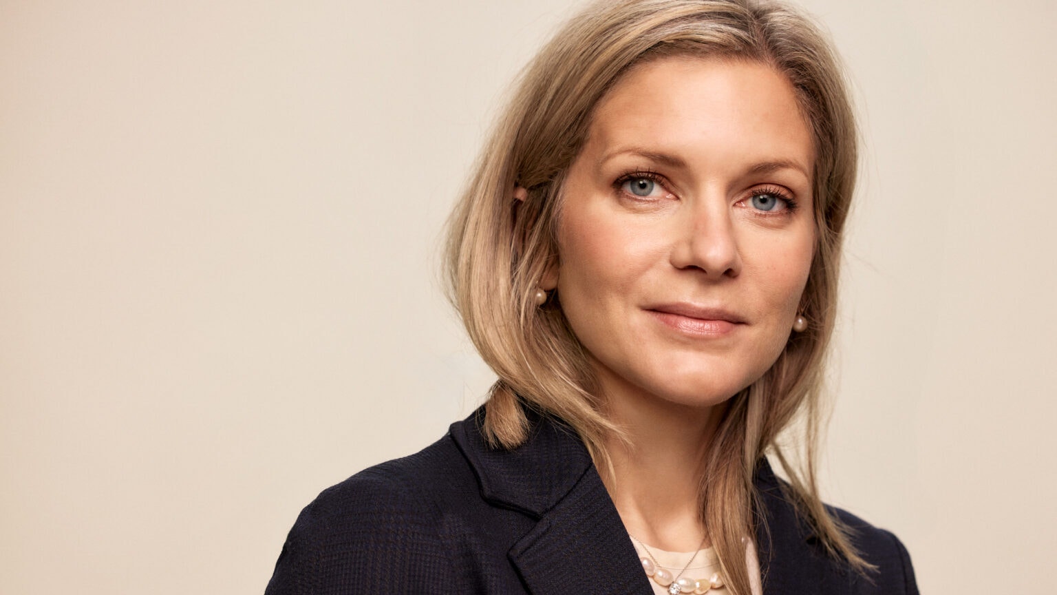 Porträtt av en kvinna med blont hår, iklädd mörkblå blazer och vit topp.