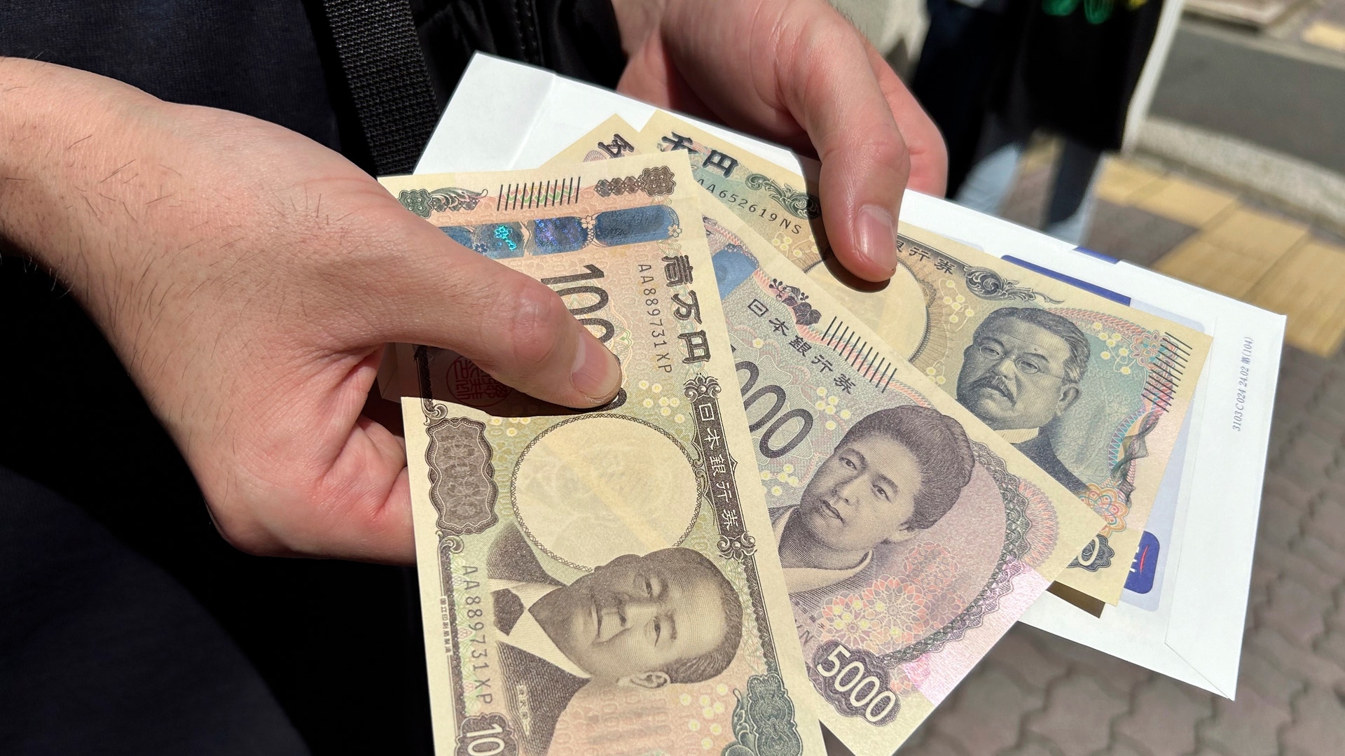 En hand håller flera japanska sedlar av olika valörer.