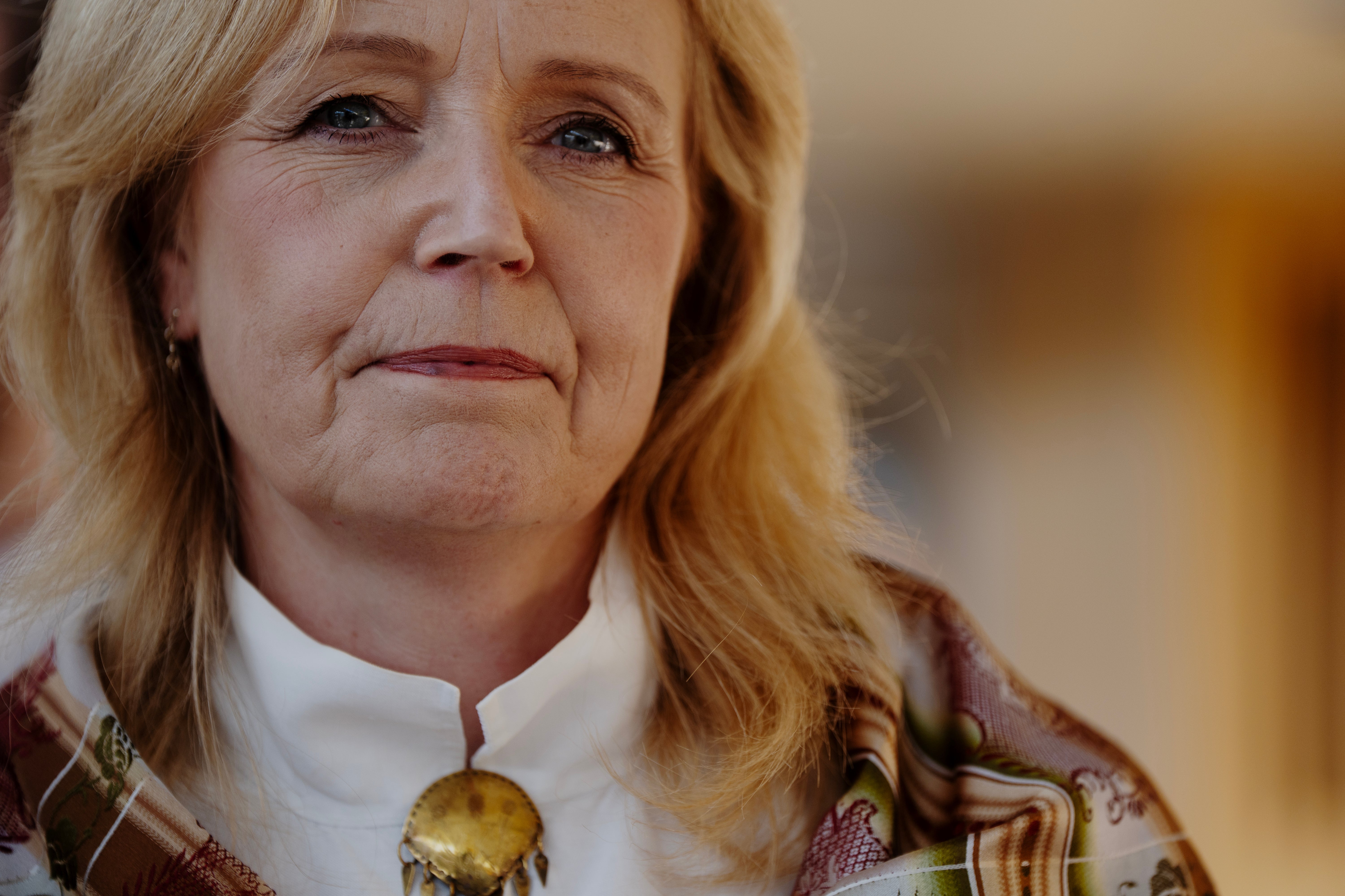 Närbild på en kvinna med blont hår som bär ett smycke och en scarf.
