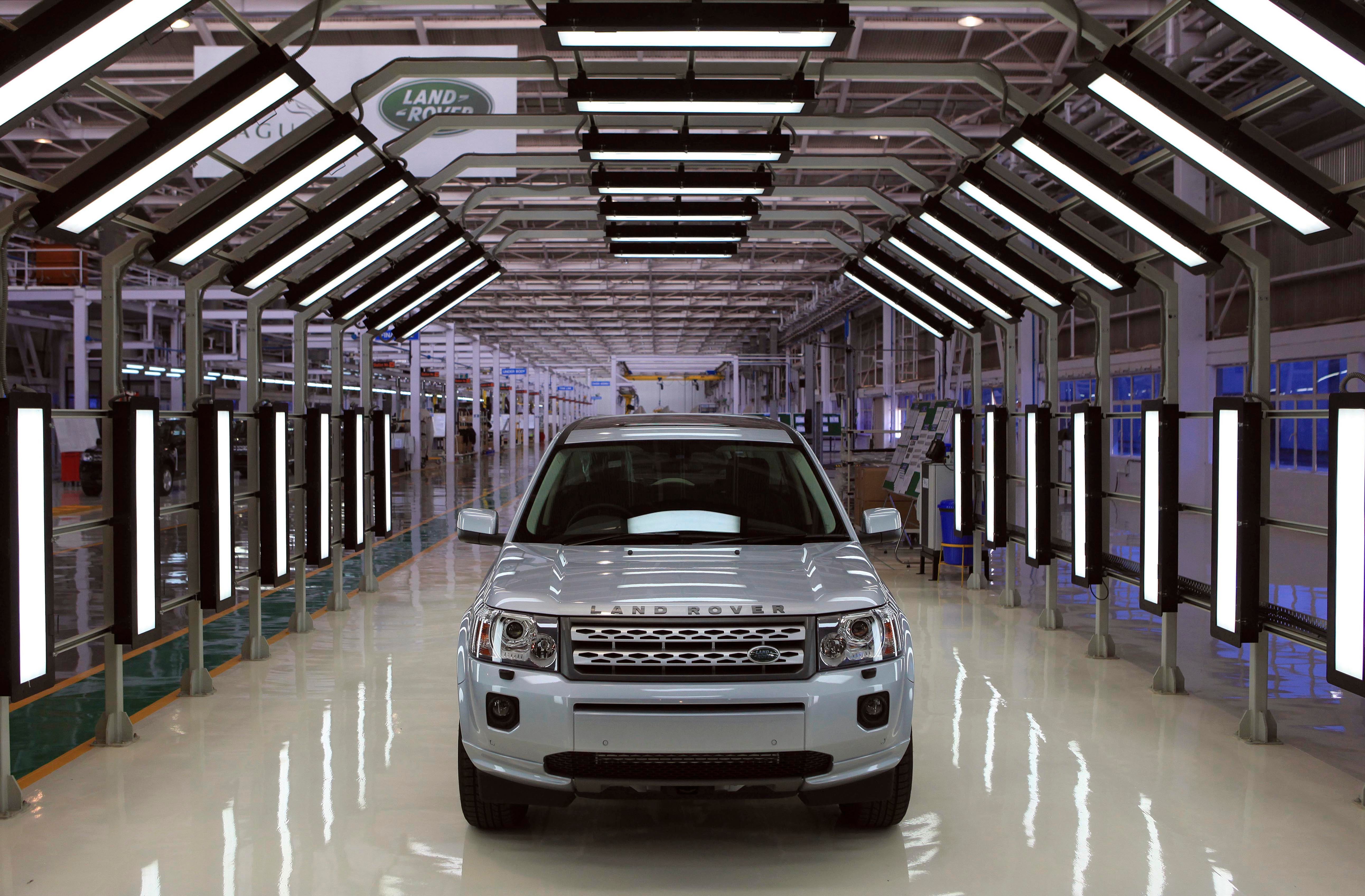 En vit Land Rover står i ett modernt fabriksgarage med LED-belysning längs väggarna.