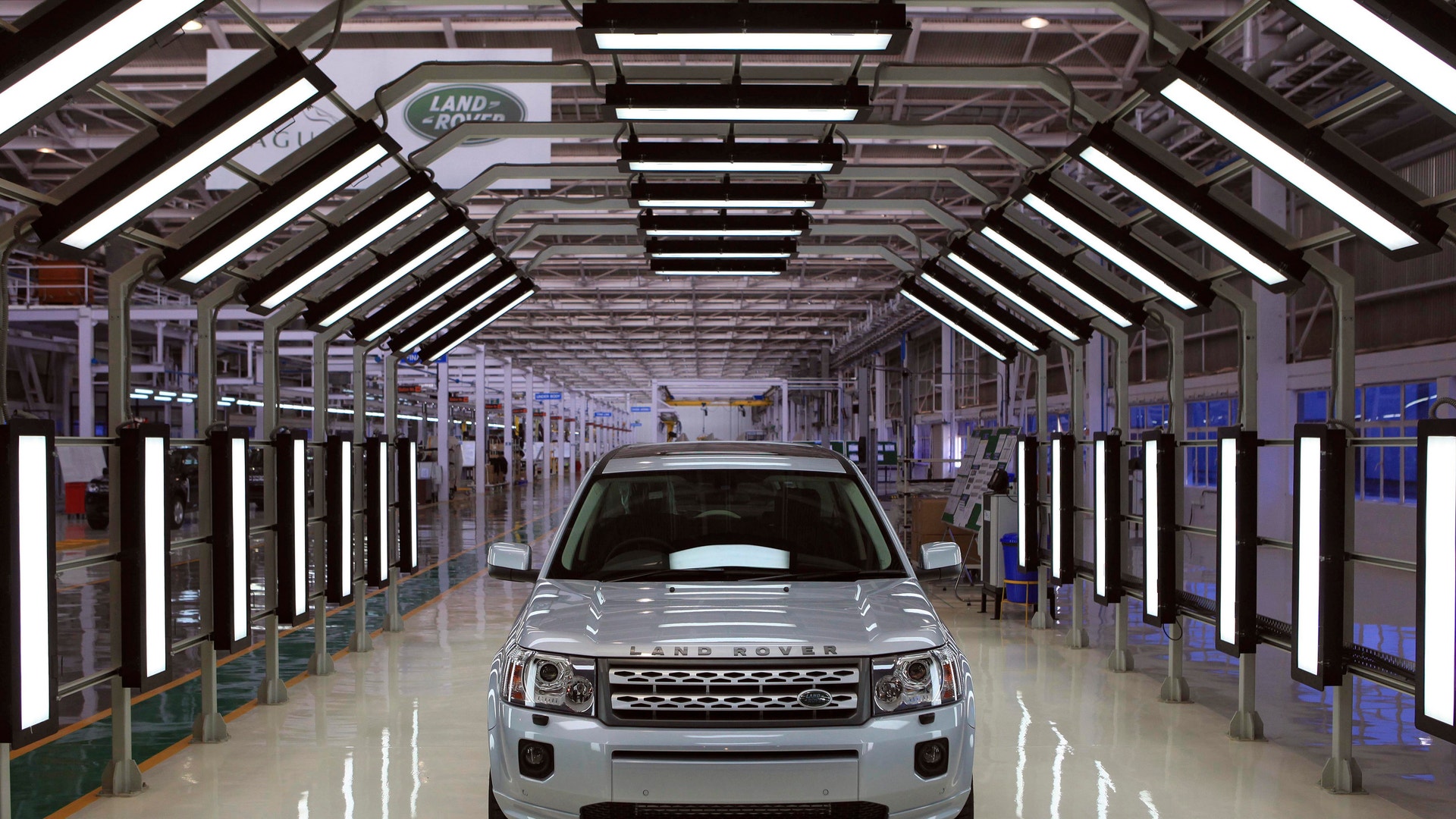 En vit Land Rover står i ett modernt fabriksgarage med LED-belysning längs väggarna.